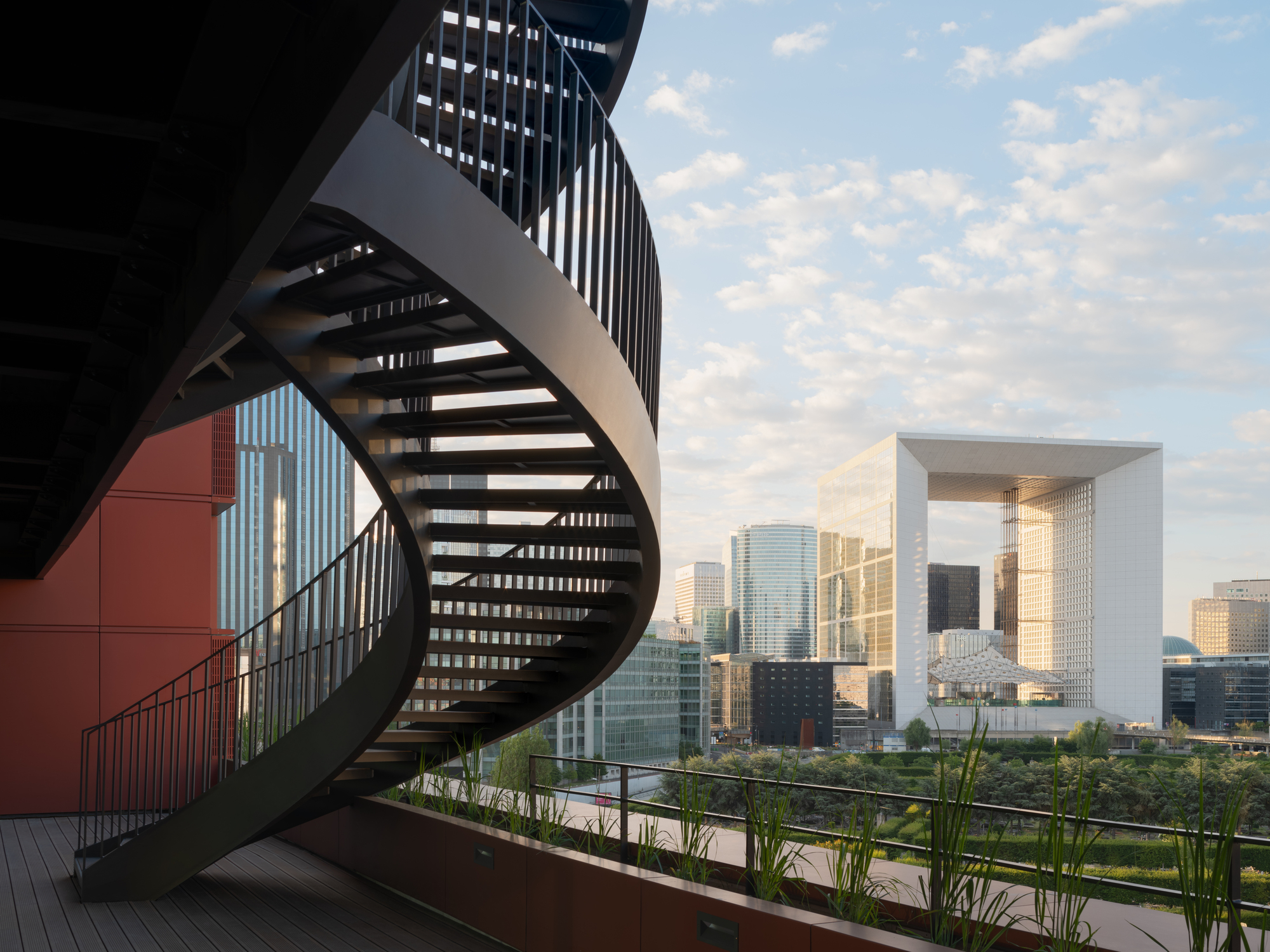 Rooftop terrace with curved steel staircase and planters overlooking the skyline in afternoon light