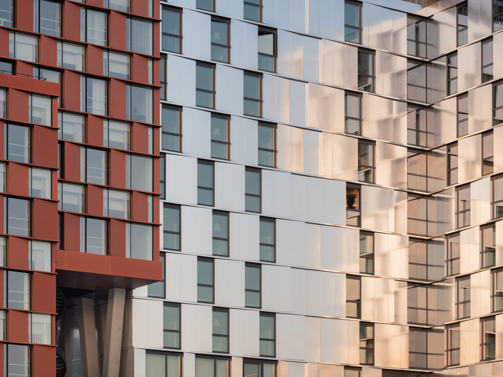 Corner junction of two facades showing terracotta and white panel grids in warm afternoon light