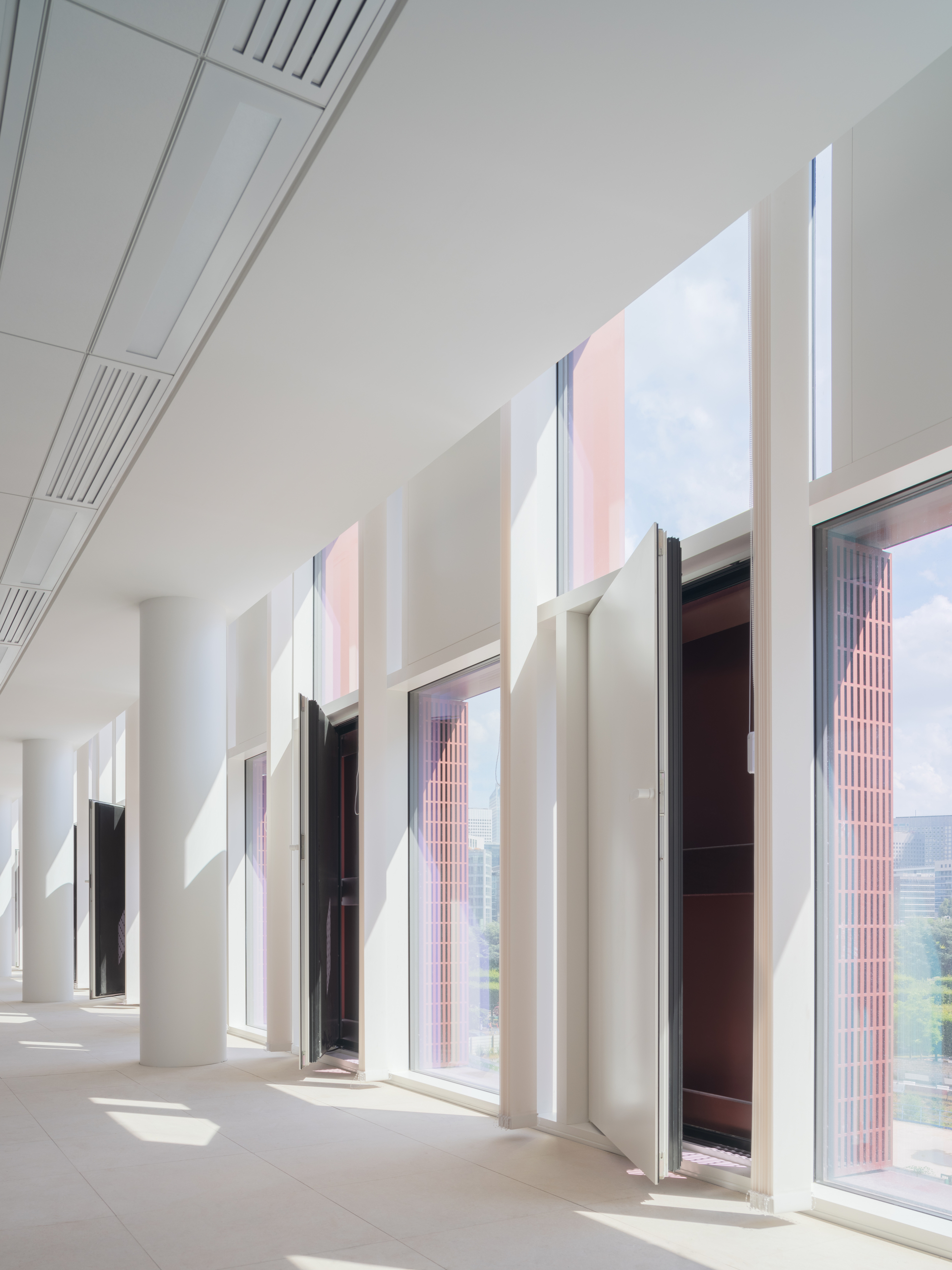 White corridor with deep-set windows and column coffers casting afternoon shadows across the floor