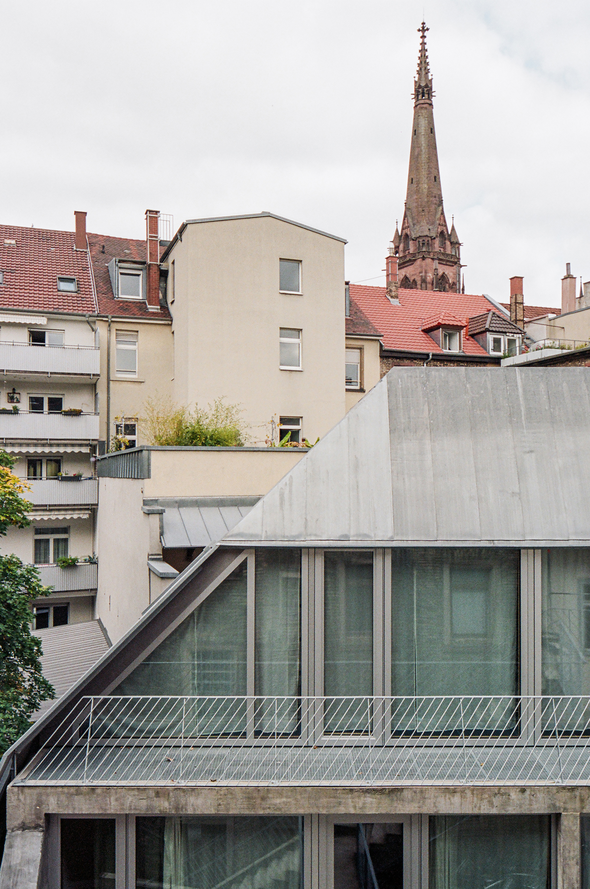 Rooftop view of the angled concrete volume with metal railings against a church spire beyond