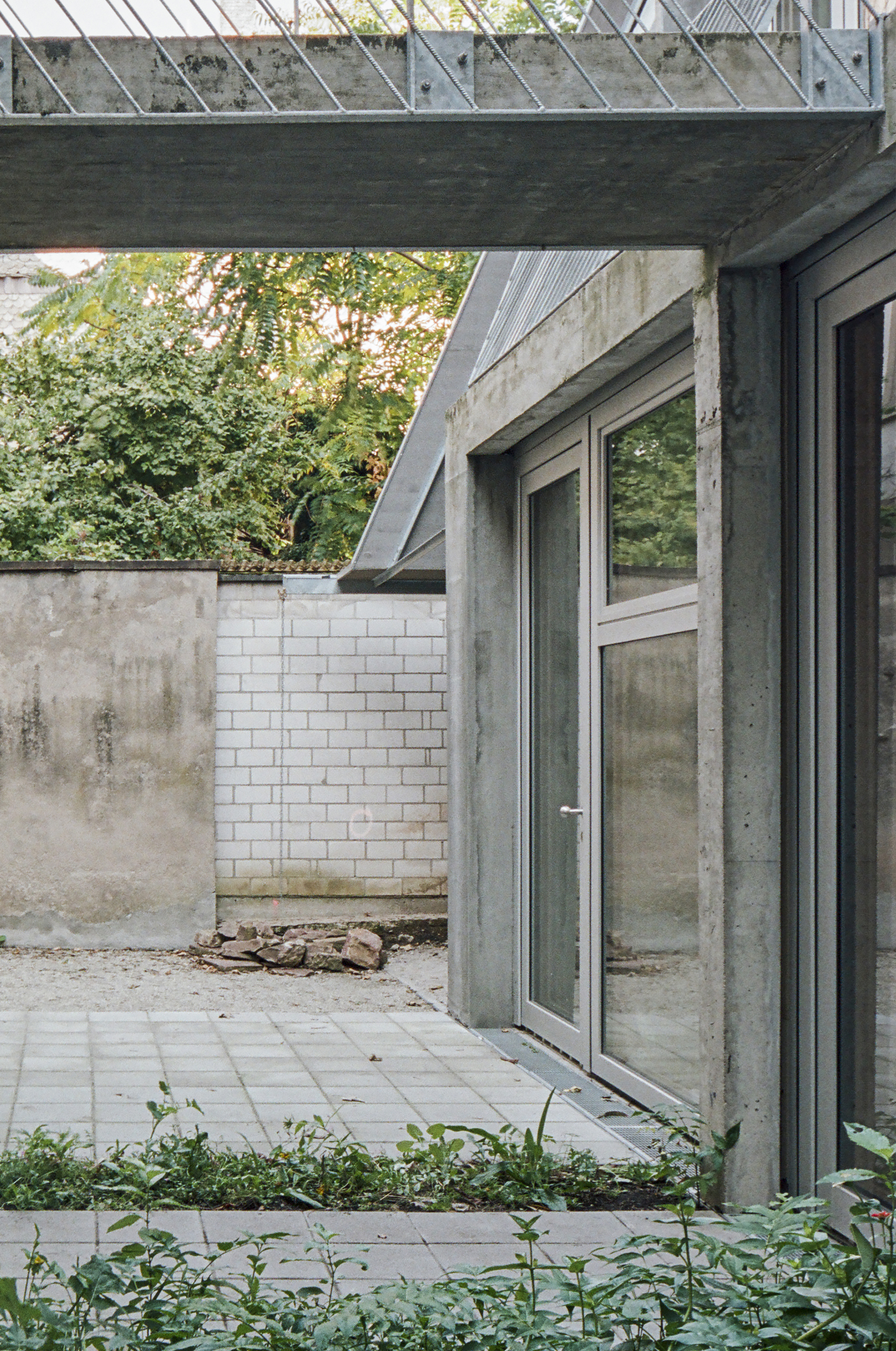 Courtyard terrace with concrete doorframe, white brick wall, and overhead metal grating in afternoon light