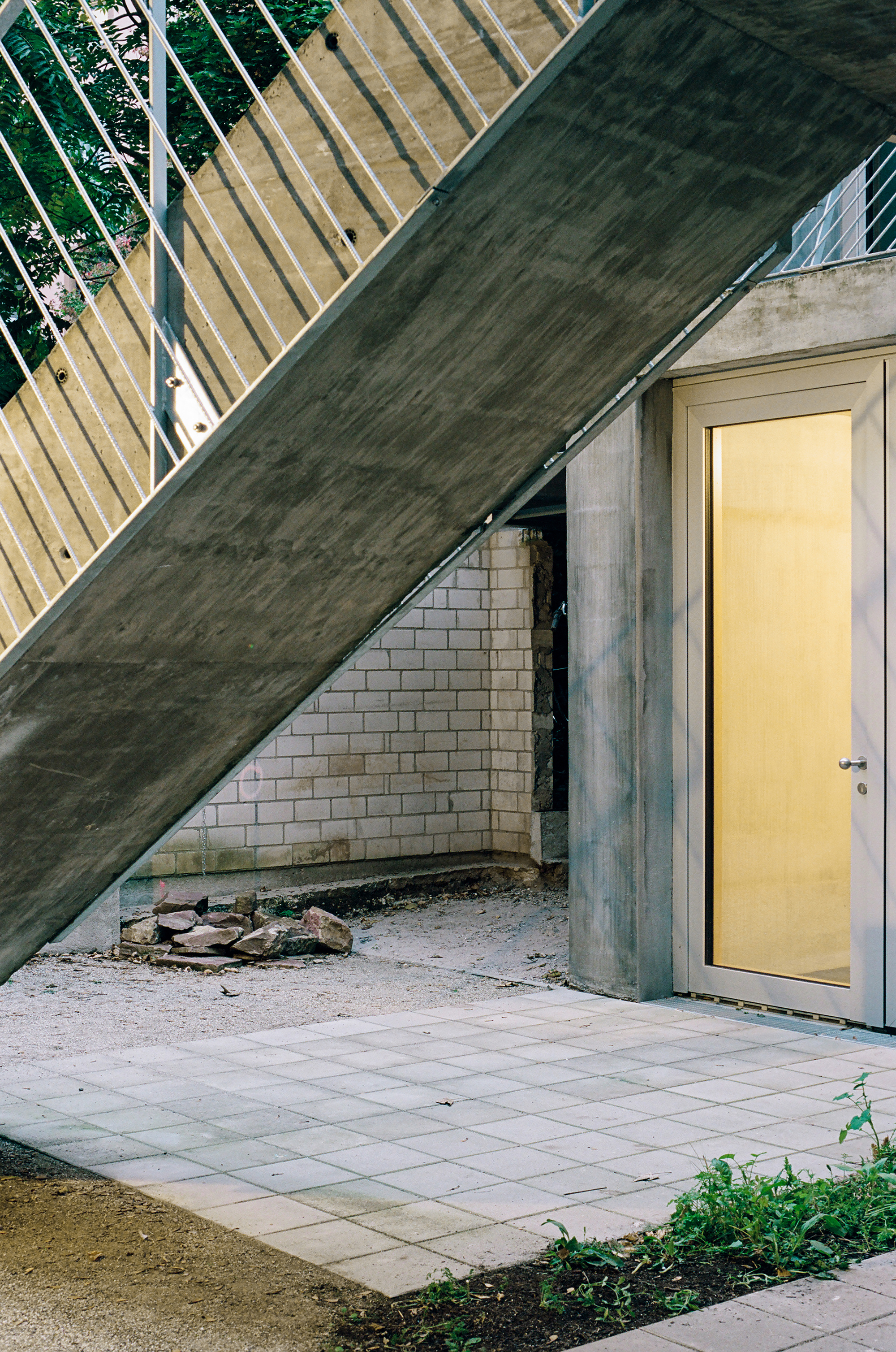 Exterior entry niche with paver courtyard beneath a sloping concrete roof and exposed brick wall