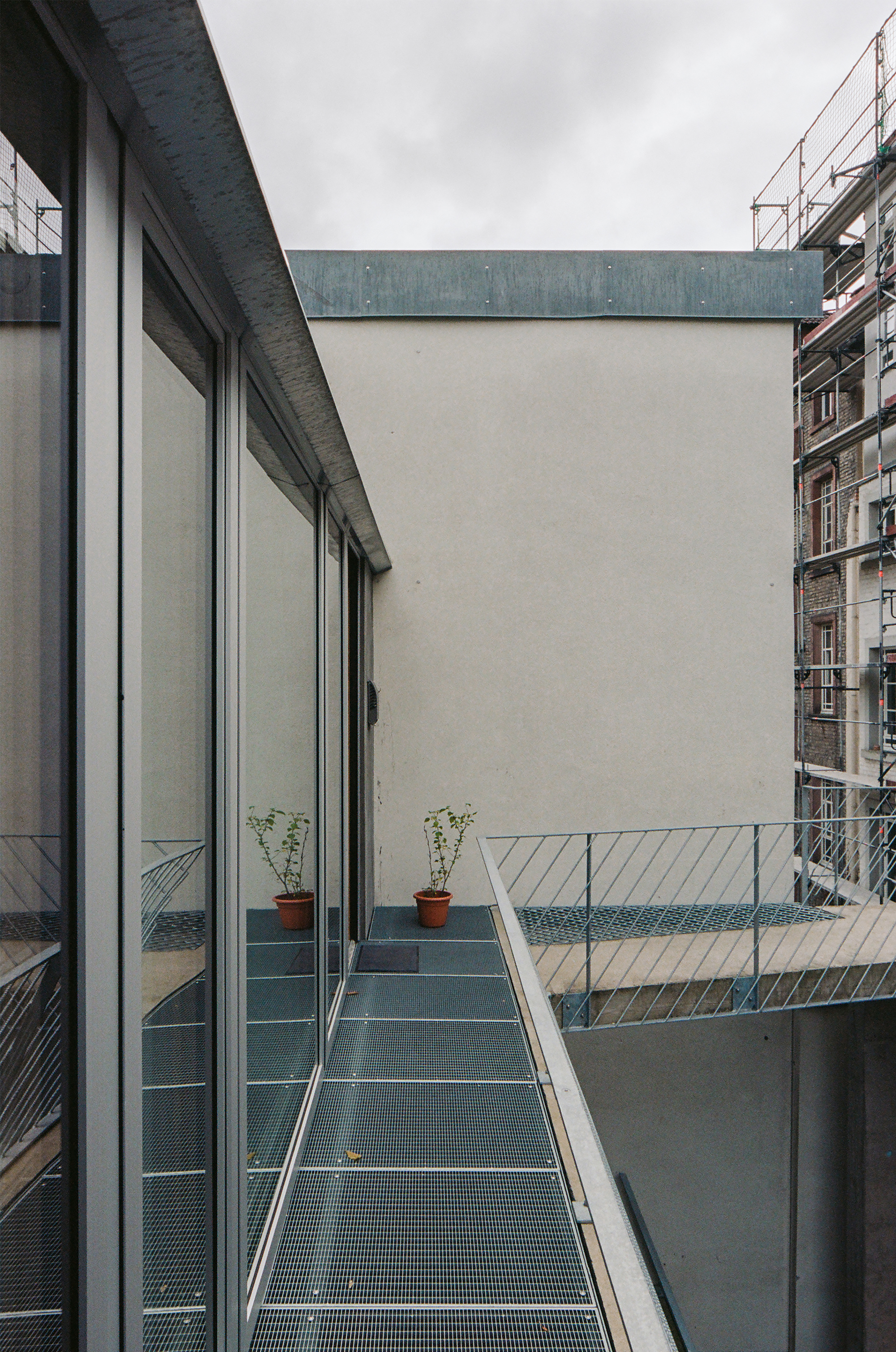 Metal grate walkway with potted plants and white railing under an overcast sky