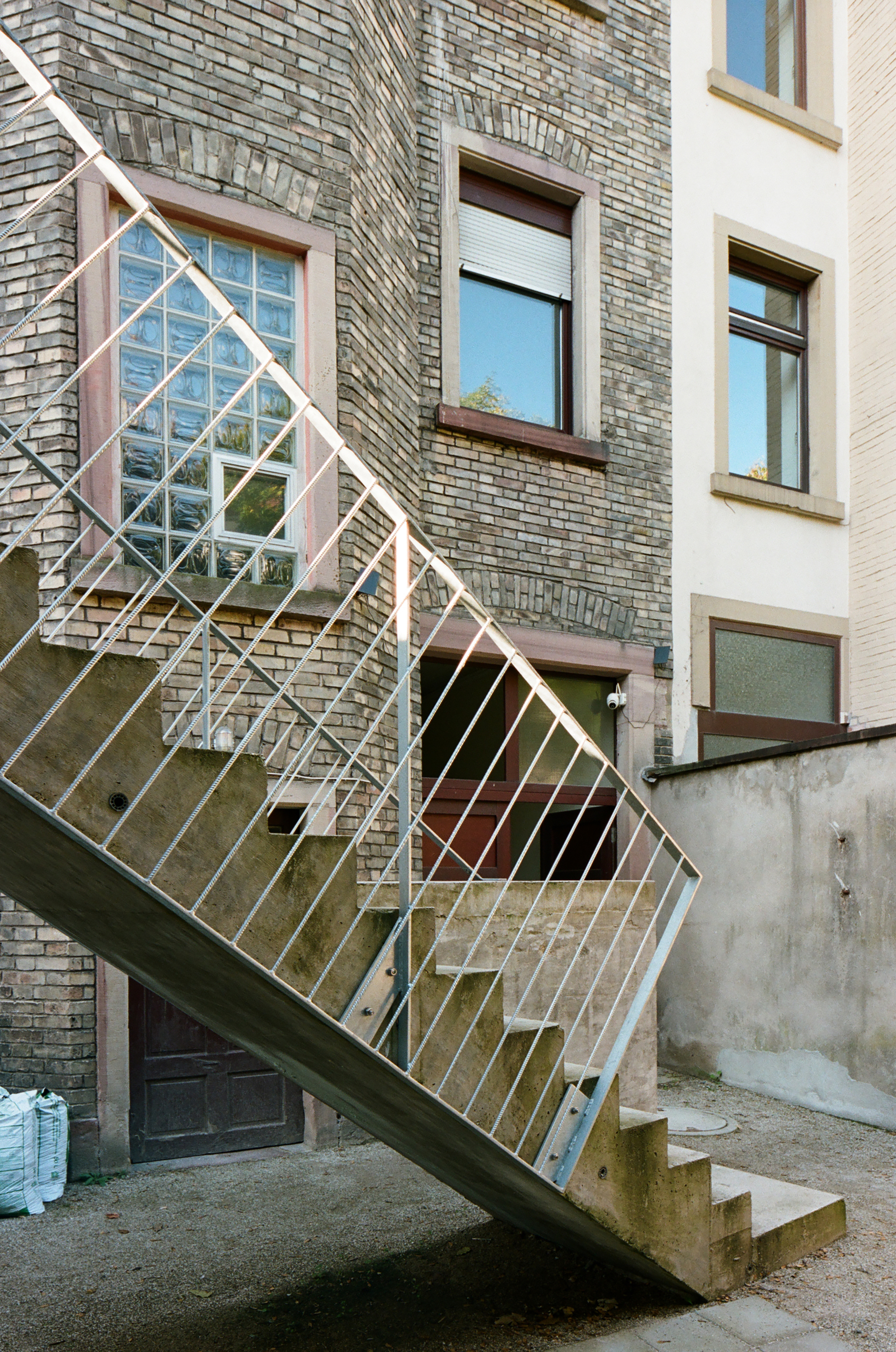 Diagonal view of steel staircase with white railings rising against grey brick facade with pink window frames