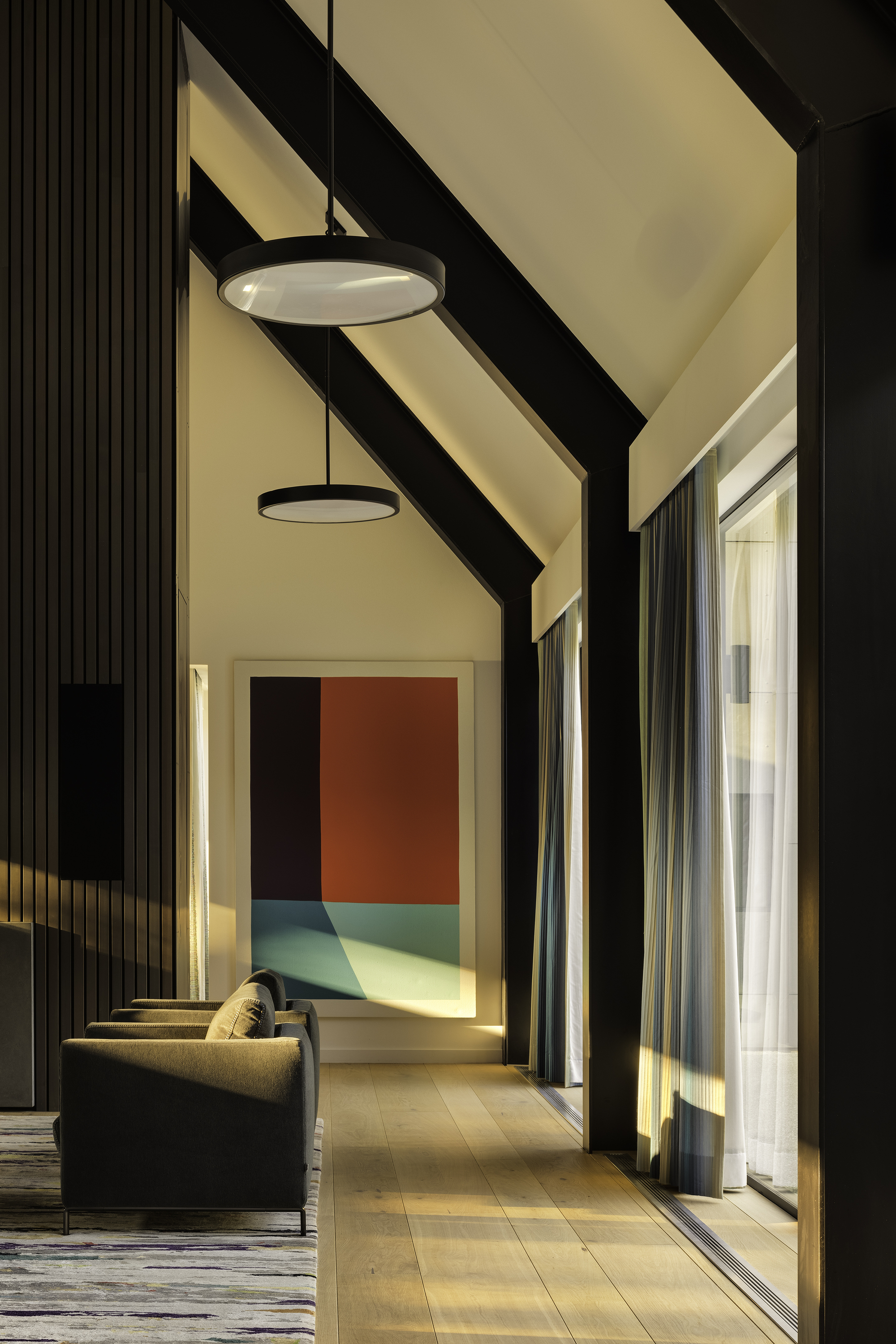 Corridor with exposed black rafters and warm afternoon light streaming through glazed walls