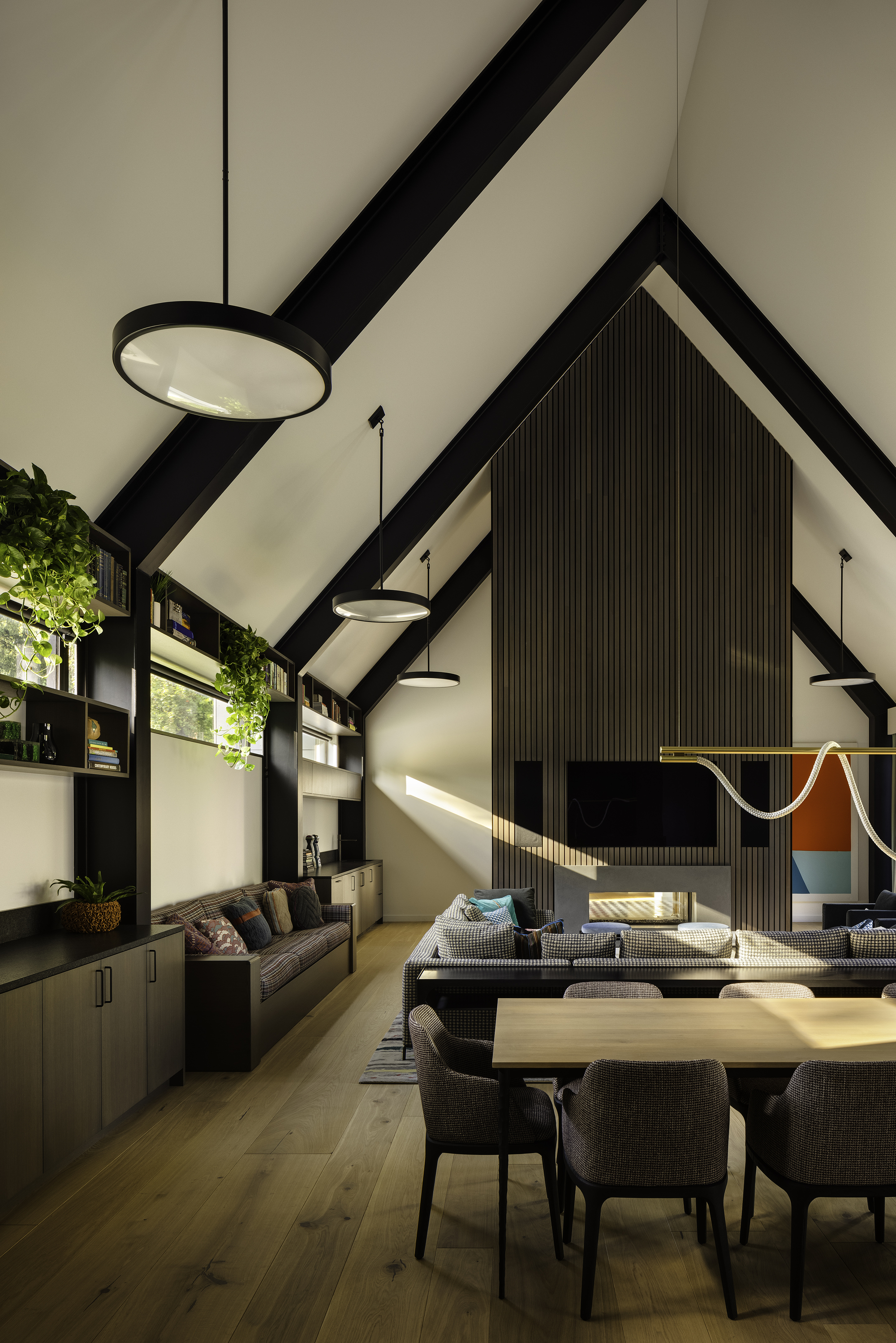 Open-plan living and dining space with black timber trusses and ribbed accent wall catching afternoon sun