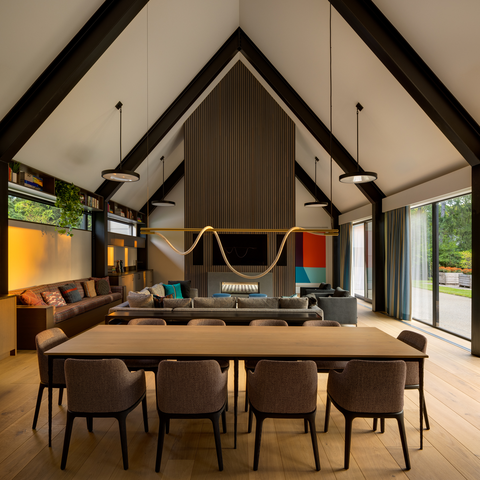 Dining table in front of vertical timber slat wall with embedded fireplace and television at dusk