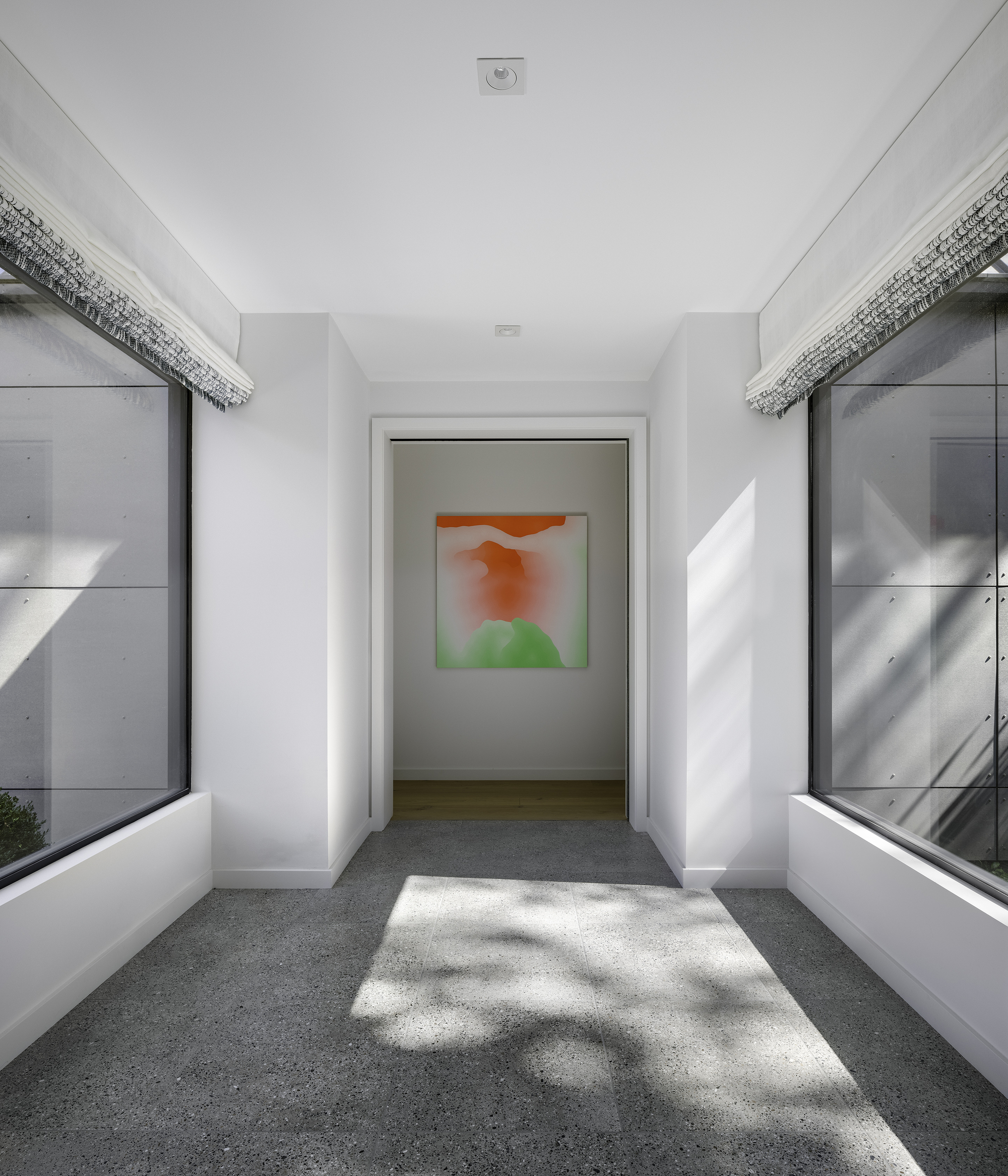 White corridor with flanking windows and dappled sunlight falling across the terrazzo floor