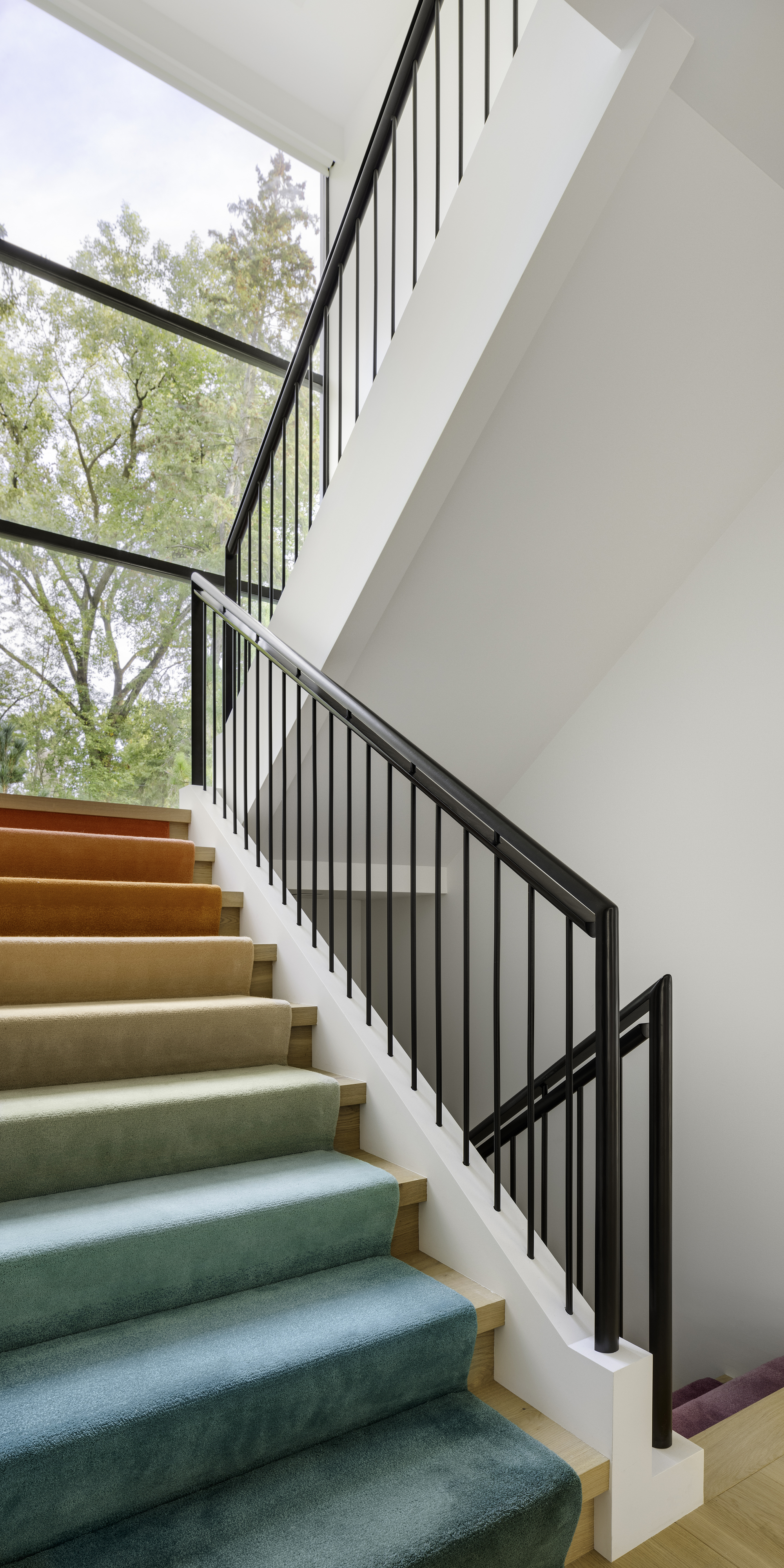 Staircase with gradient-colored runner from green to purple and black metal railing beside tall windows
