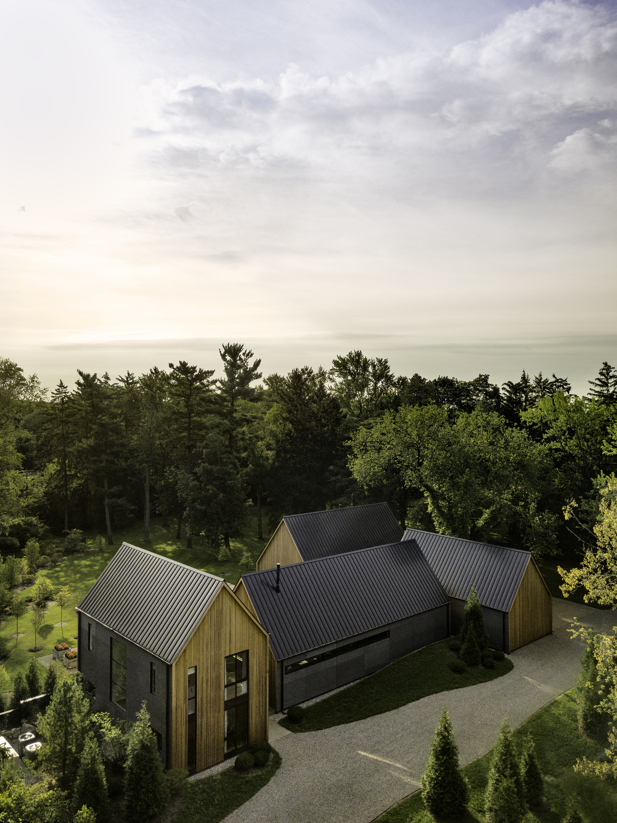Aerial view of clustered gabled volumes with metal roofs set against a forested hillside