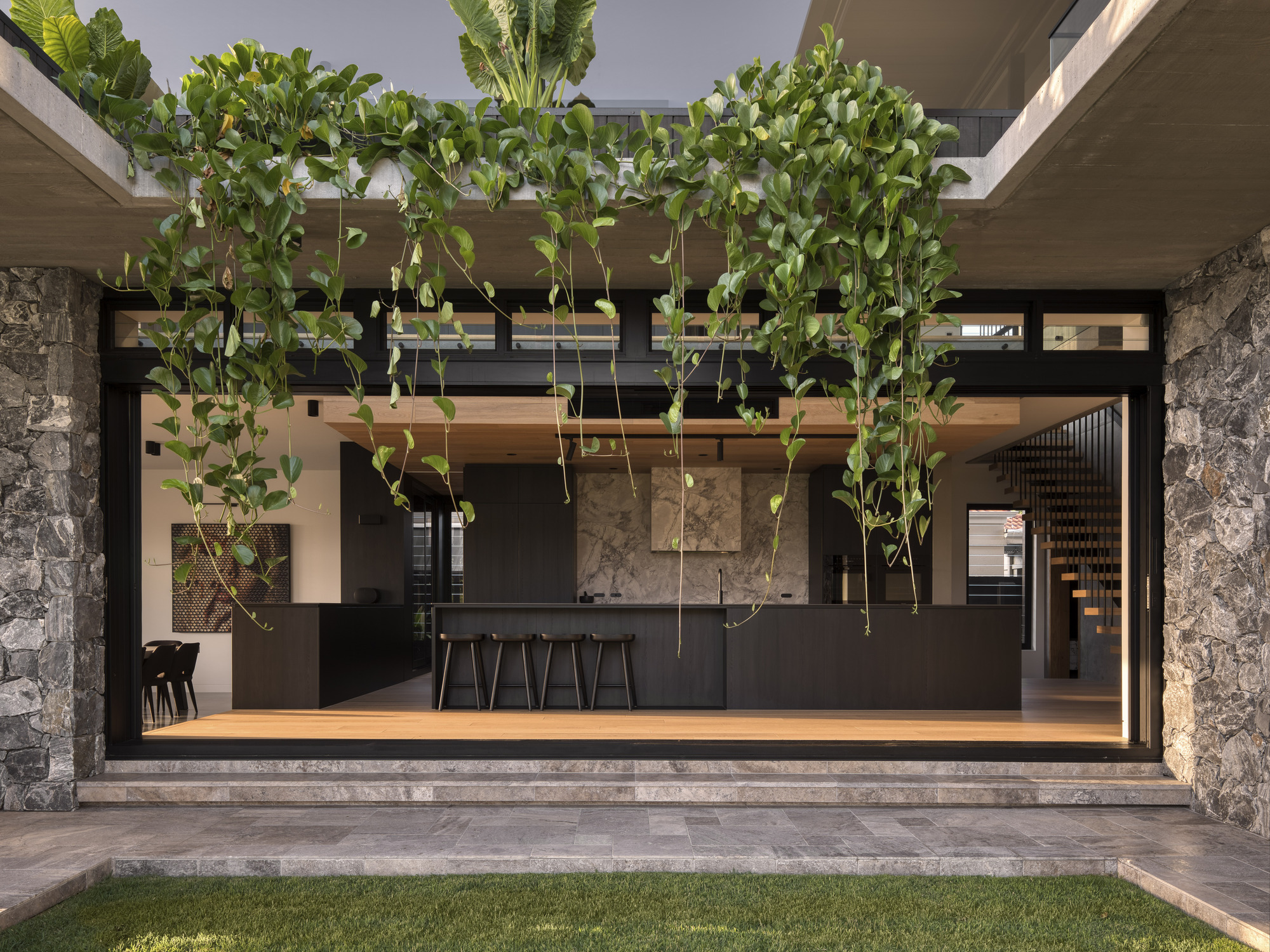 View into the open kitchen with hanging vines, stone columns and dark cabinetry from the courtyard