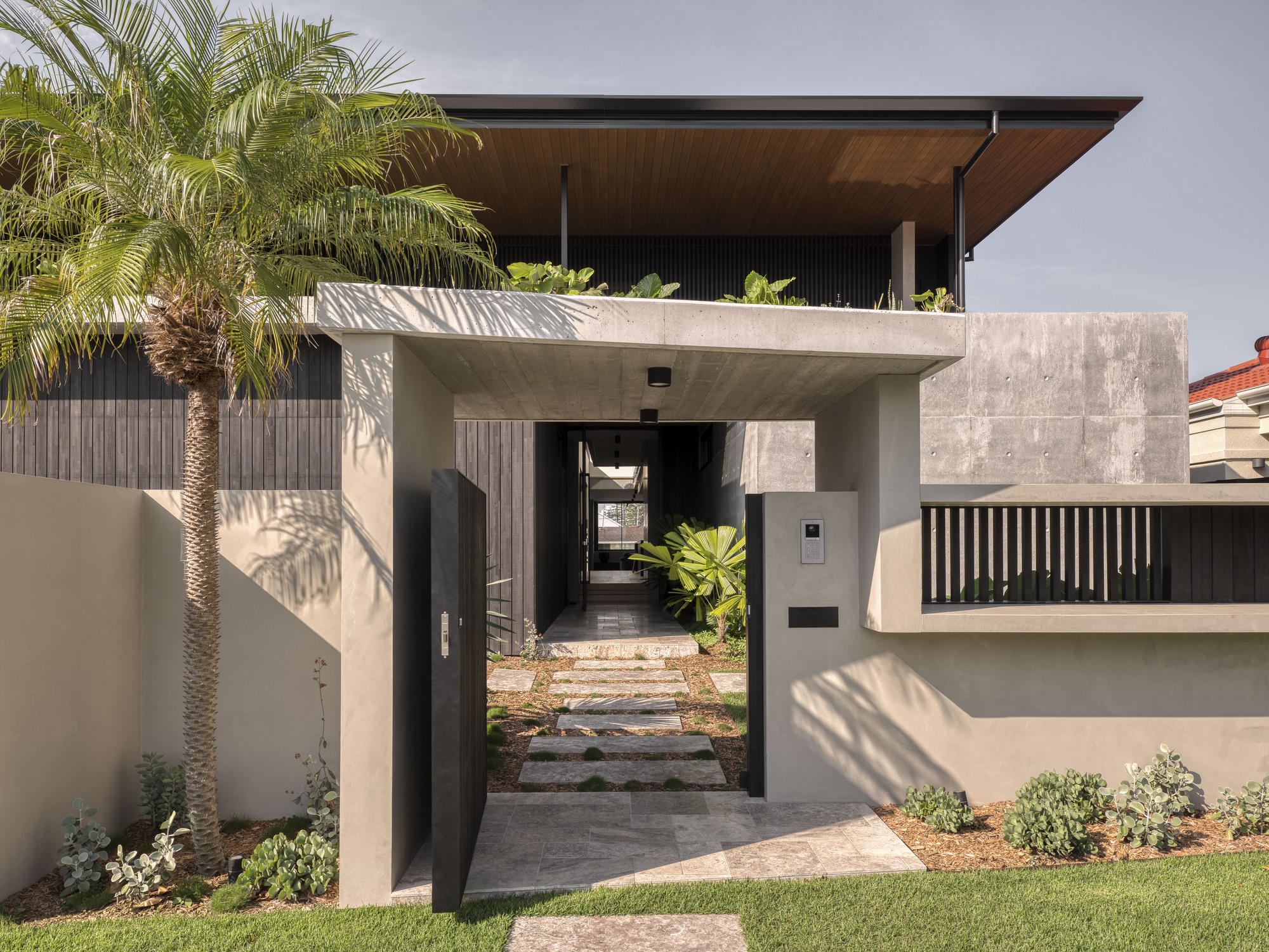 Entry portal with concrete canopy, stepping stones and palm tree casting afternoon shadows