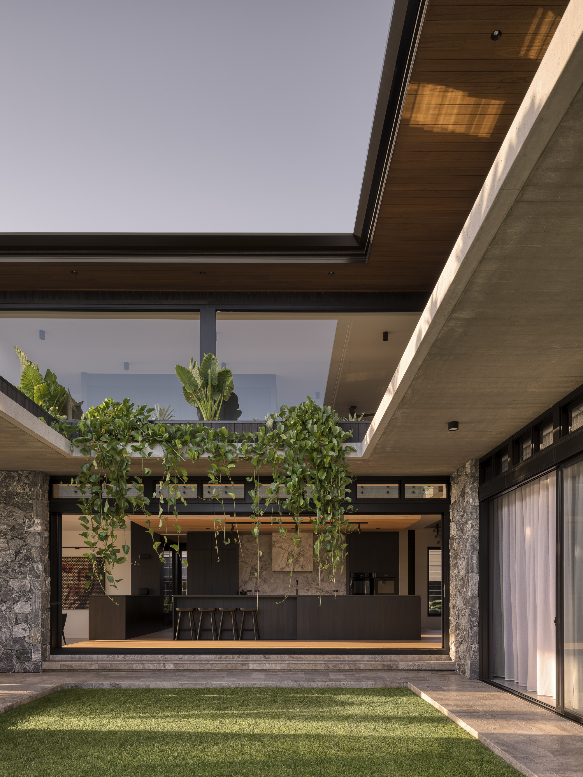 Internal courtyard with lawn, suspended planters, timber soffits and glass-walled kitchen at dusk