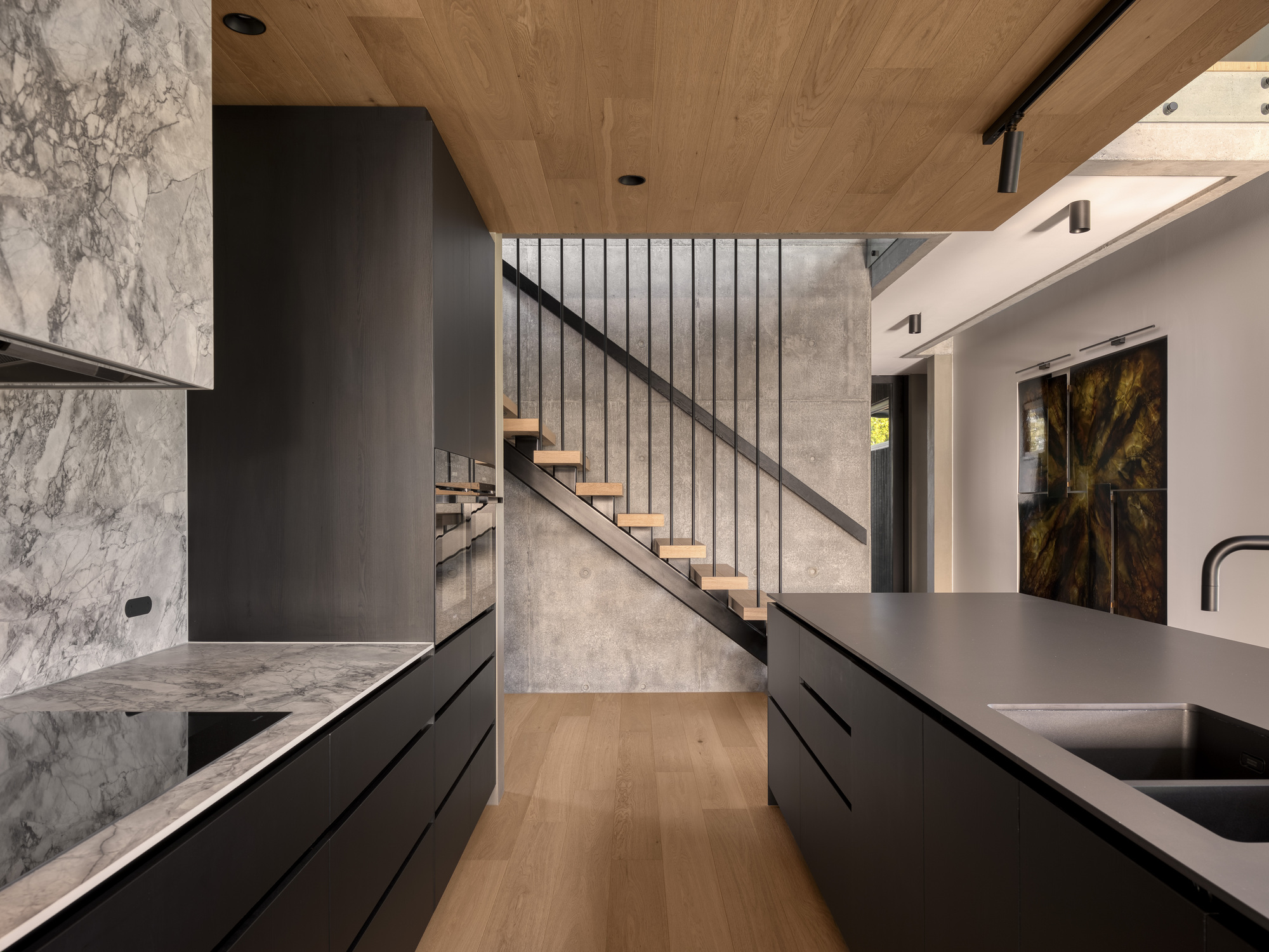 Kitchen with black cabinetry and veined marble countertop beneath timber-clad ceiling and open staircase