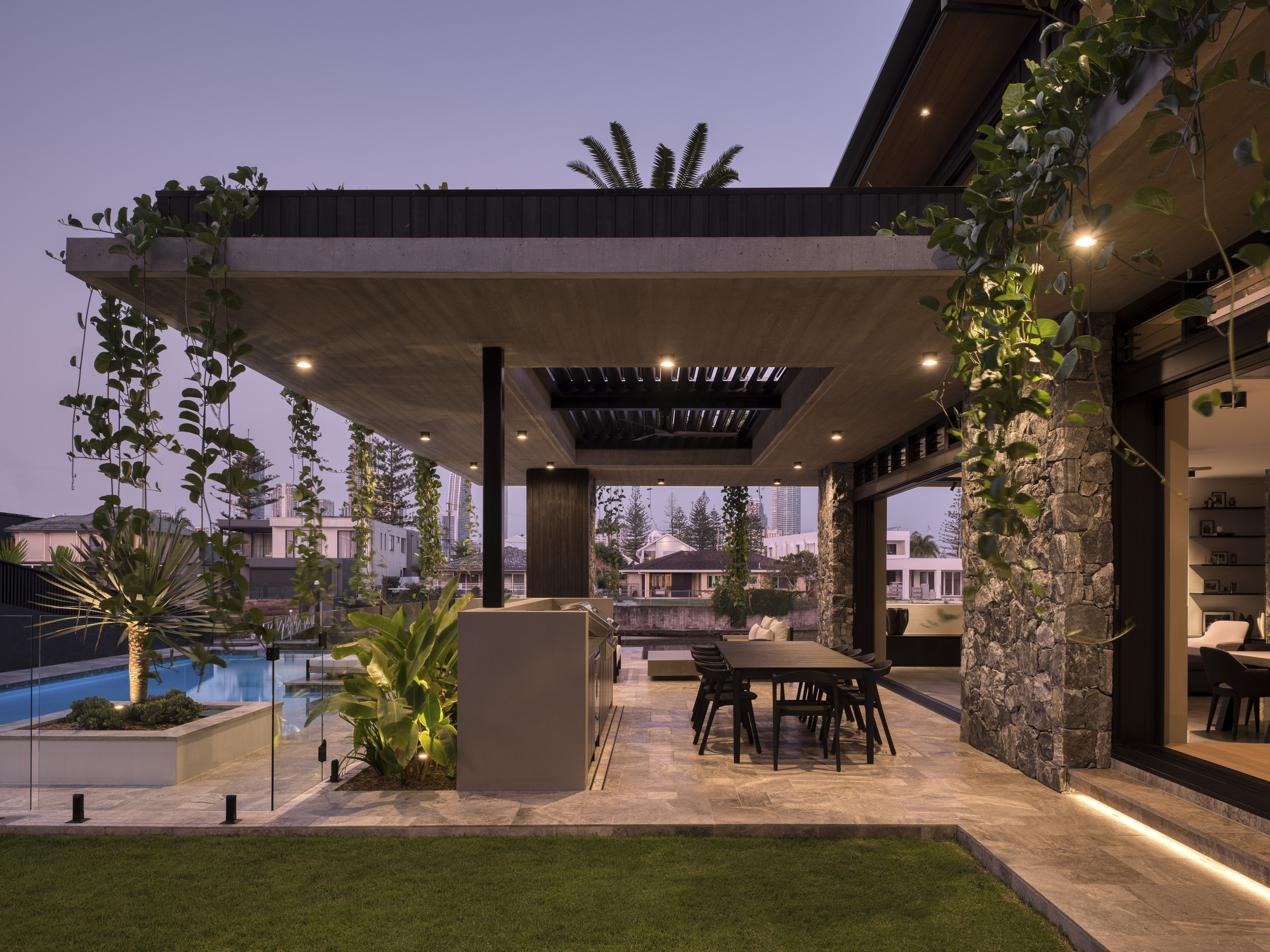 Covered outdoor dining terrace with stone columns wrapped in vines at dusk