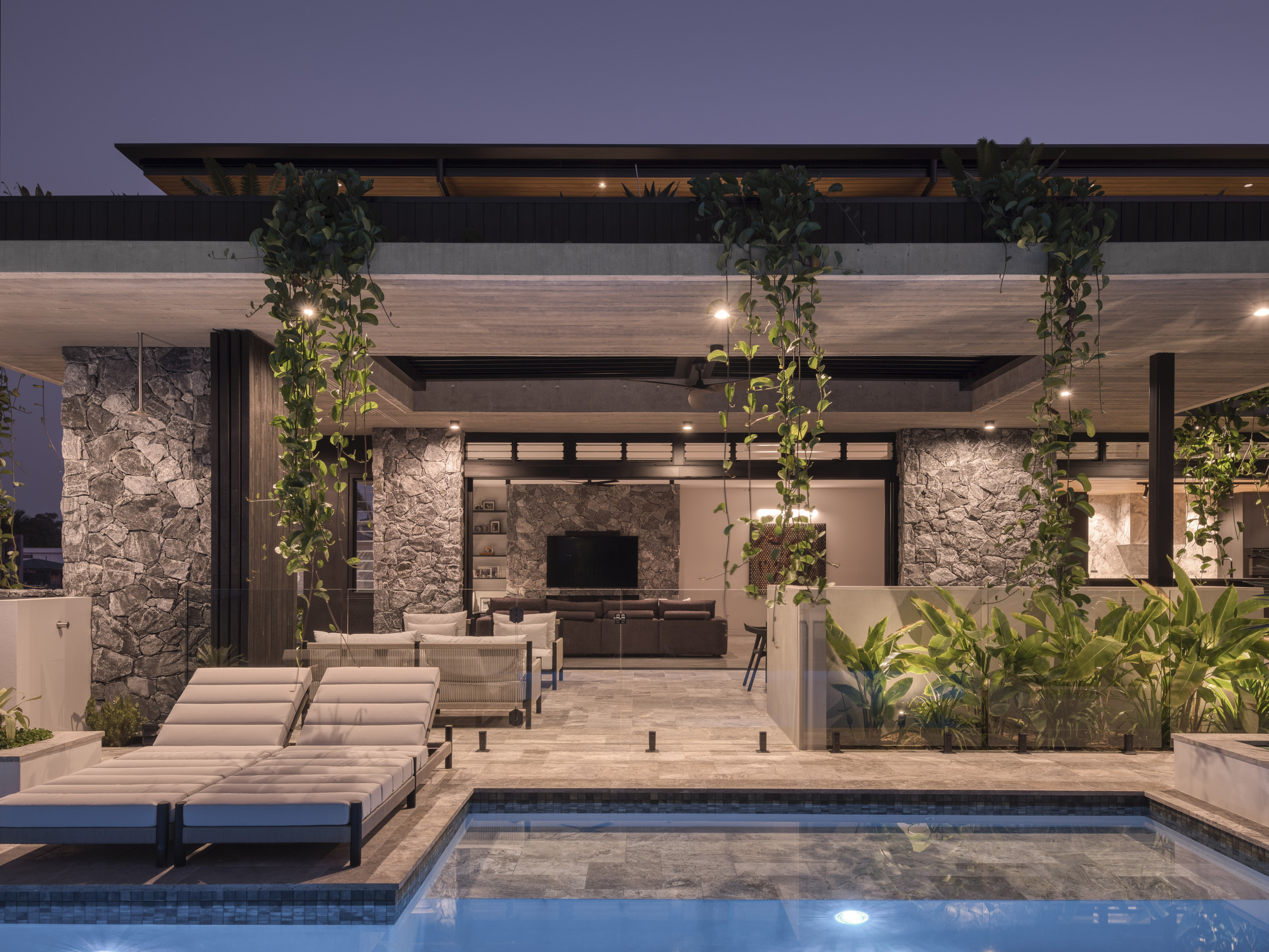 Pool deck with stone columns, hanging plants and views into living room at twilight