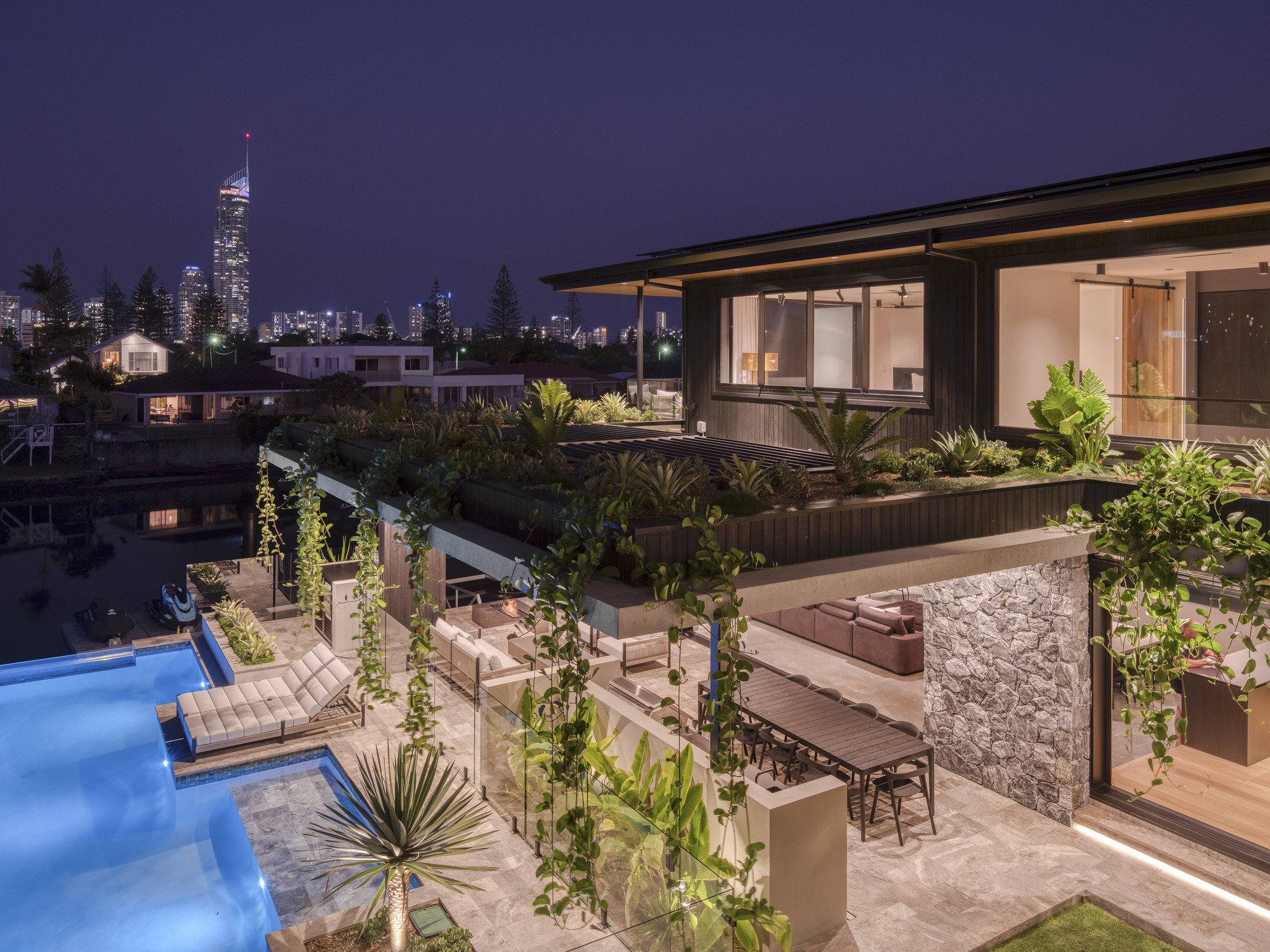 Multi-level terrace with planted beds, outdoor dining area, and pool at twilight with distant skyline
