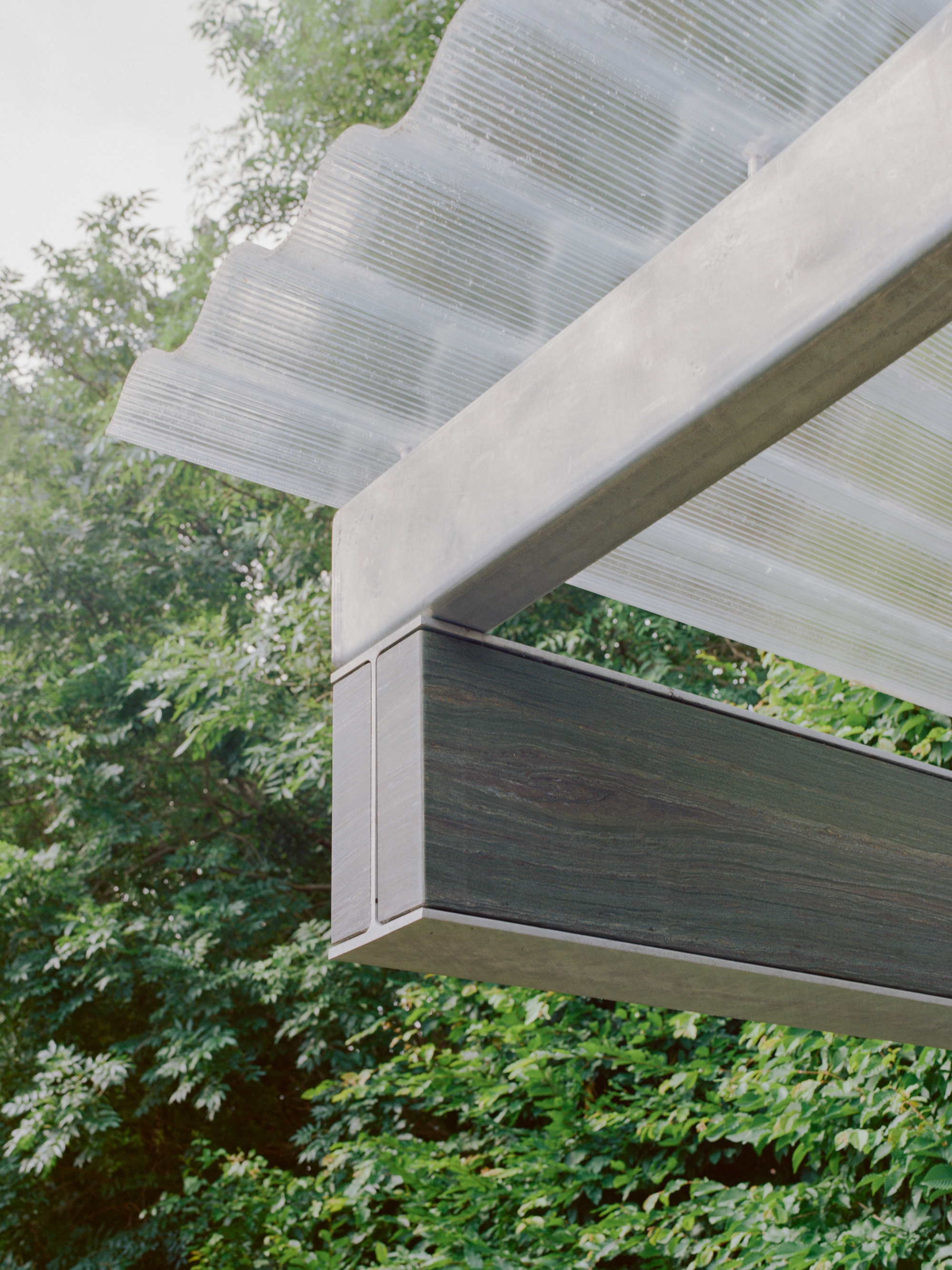 Close-up of the cantilevered beam corner showing the ribbed canopy soffit and dark timber fascia