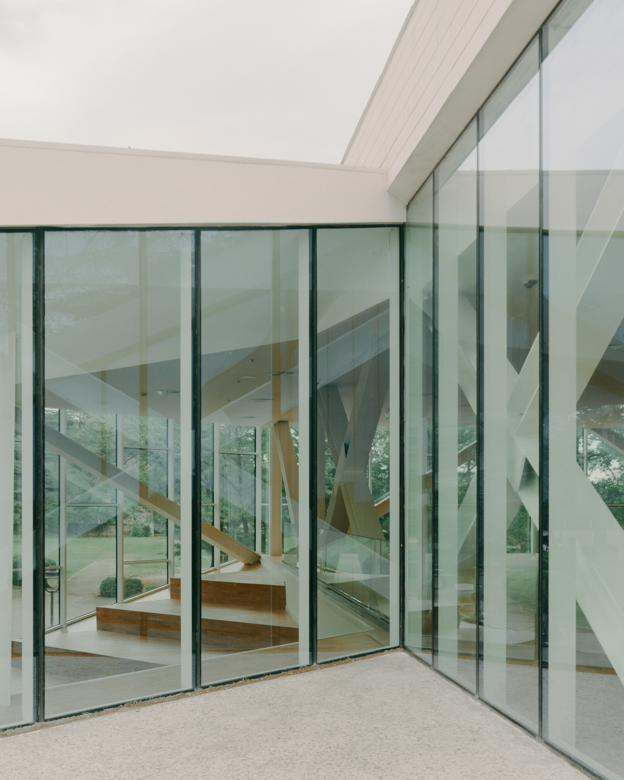 Corner courtyard enclosed by floor-to-ceiling glass walls revealing the timber staircase within