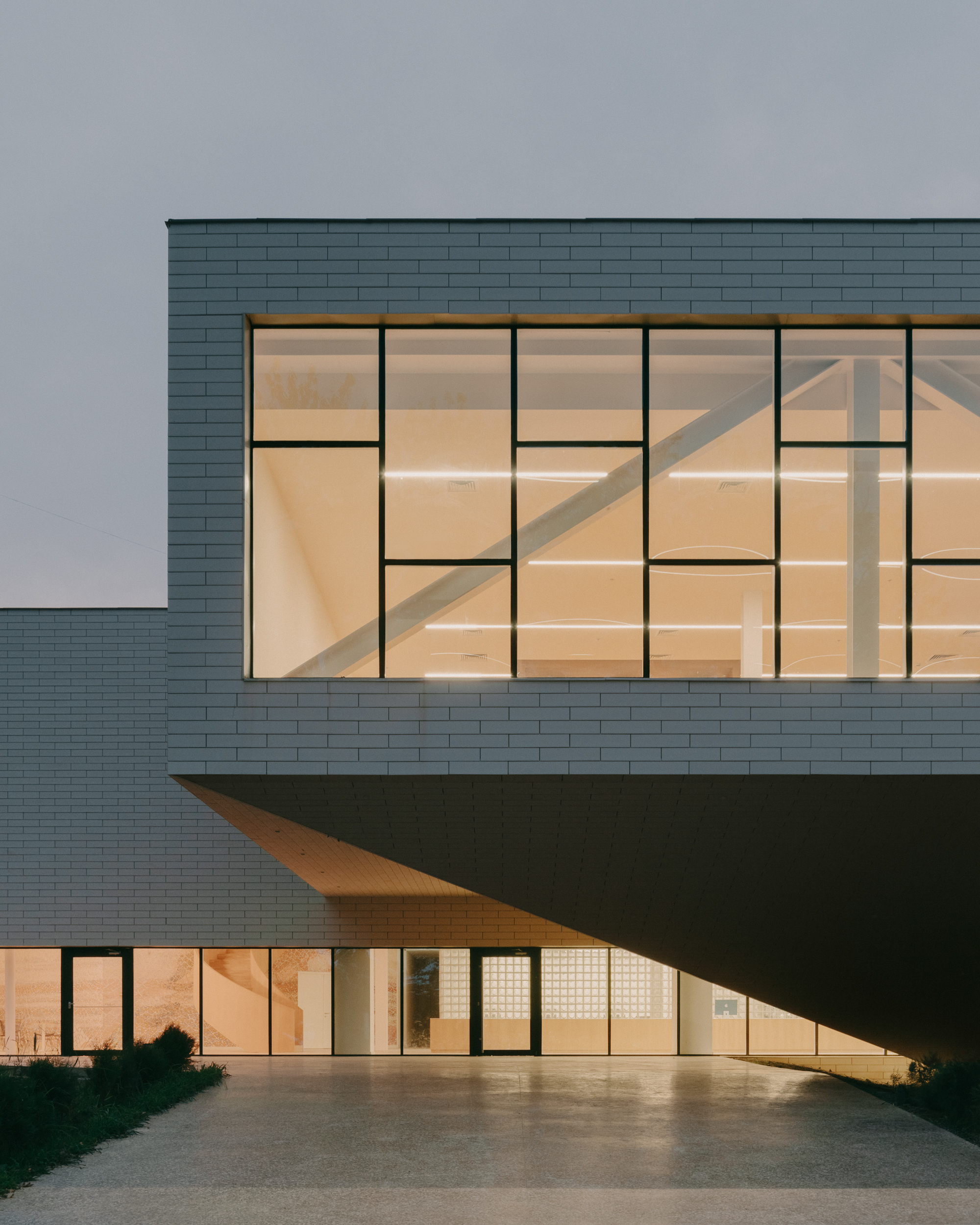 Cantilevered upper level with grid-patterned glazing illuminated at twilight above ground floor entrance