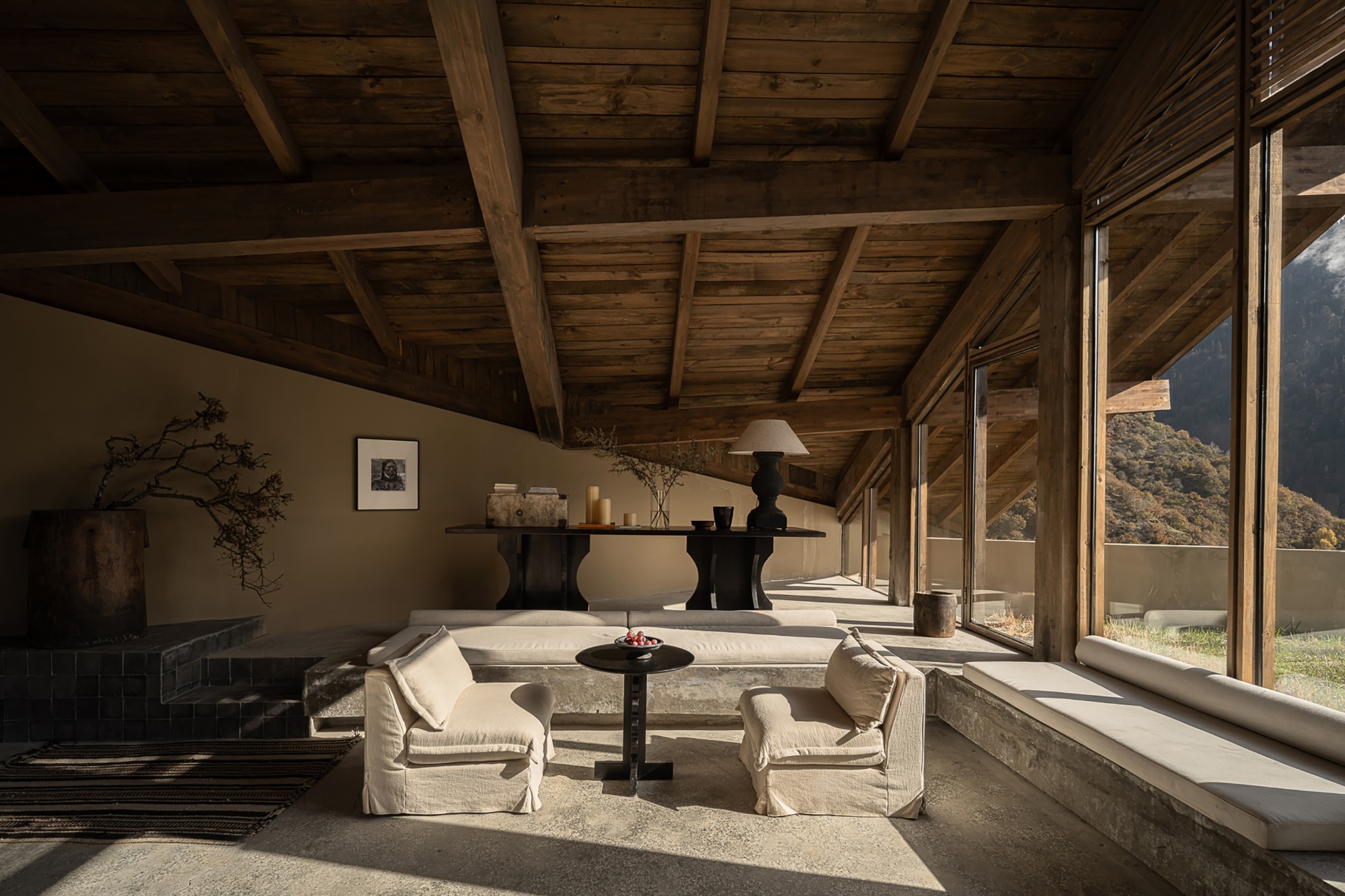 Living room with exposed timber ceiling and beams, sunken seating area, and floor-to-ceiling glazing facing mountains