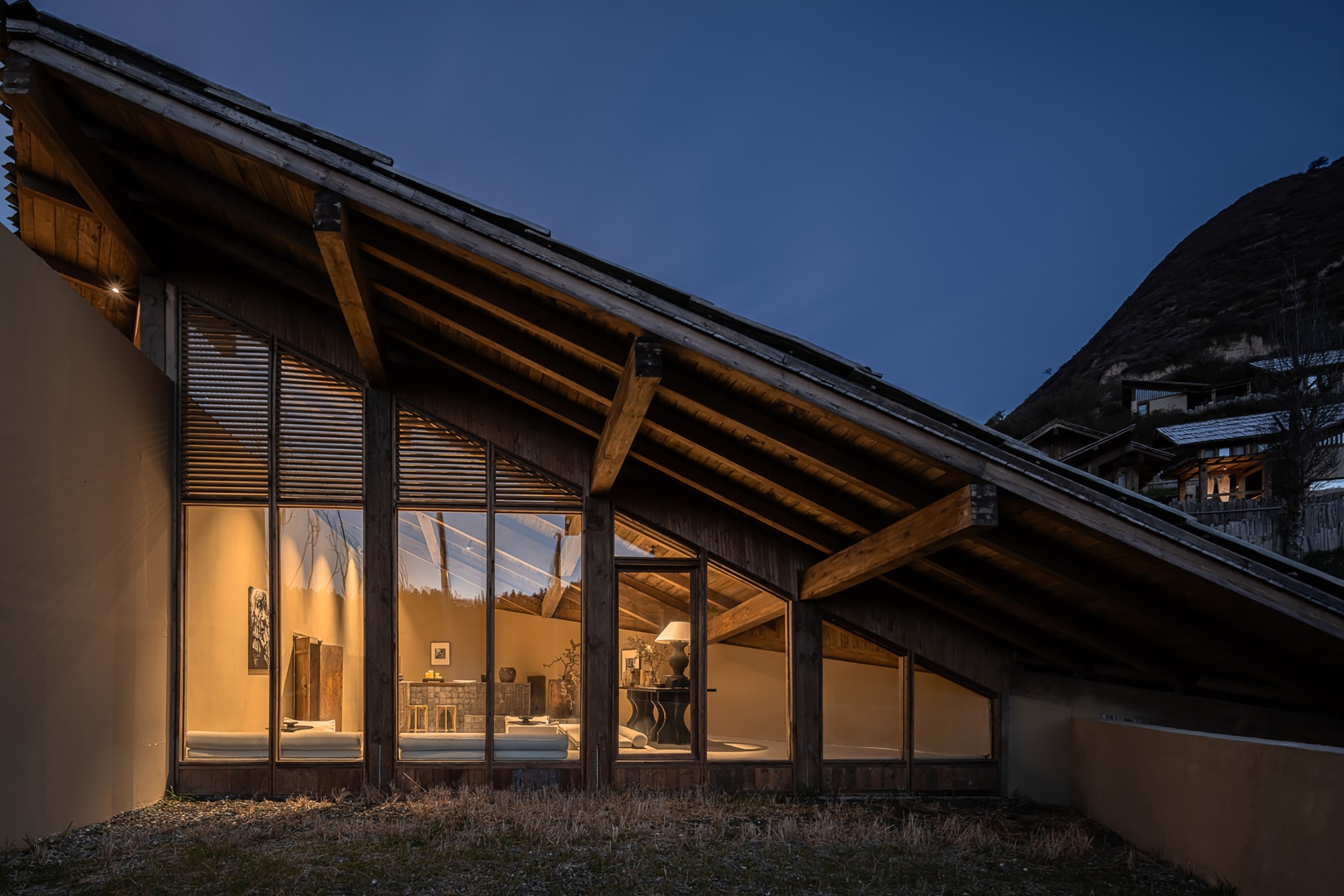 Glazed facade with exposed timber rafters illuminated against the blue evening sky