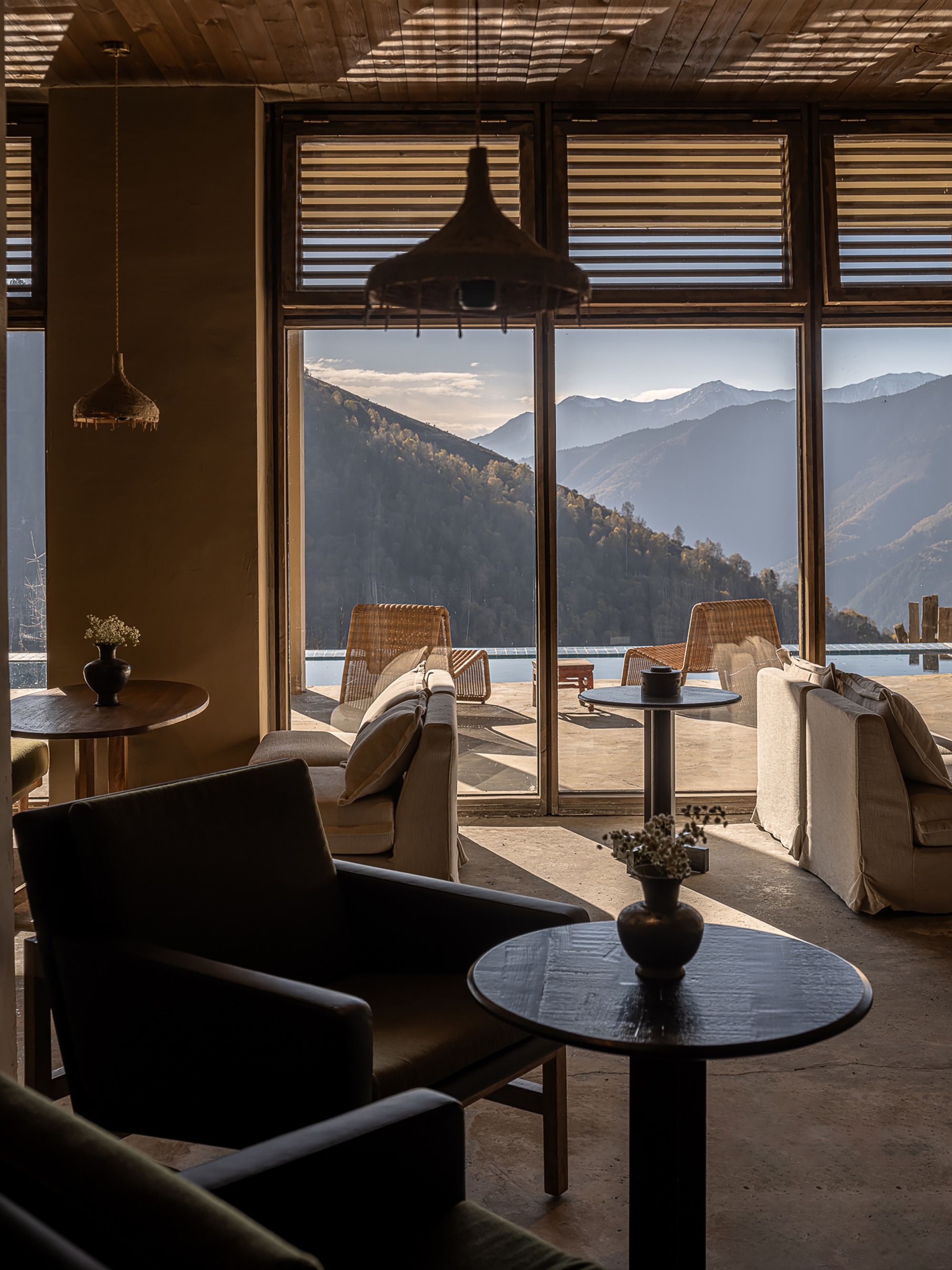 Interior lounge with timber ceiling and floor-to-ceiling windows framing layered mountain ridges