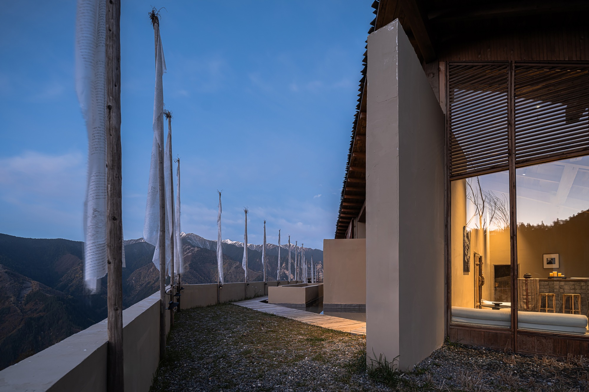 Rooftop terrace with prayer flags and gravel surface at dusk with mountain peaks in distance
