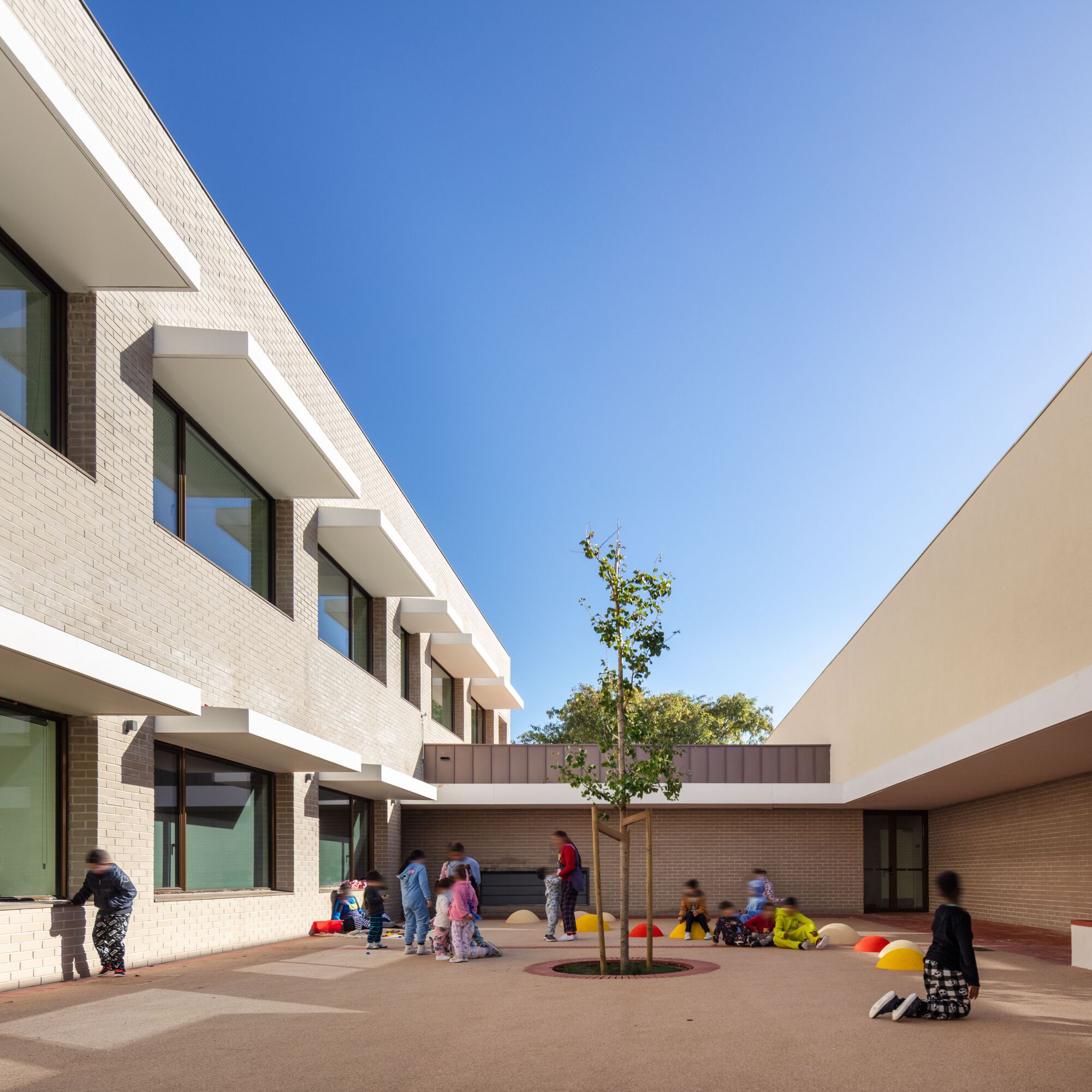Courtyard view between brick volumes with children gathered around a planted tree bed
