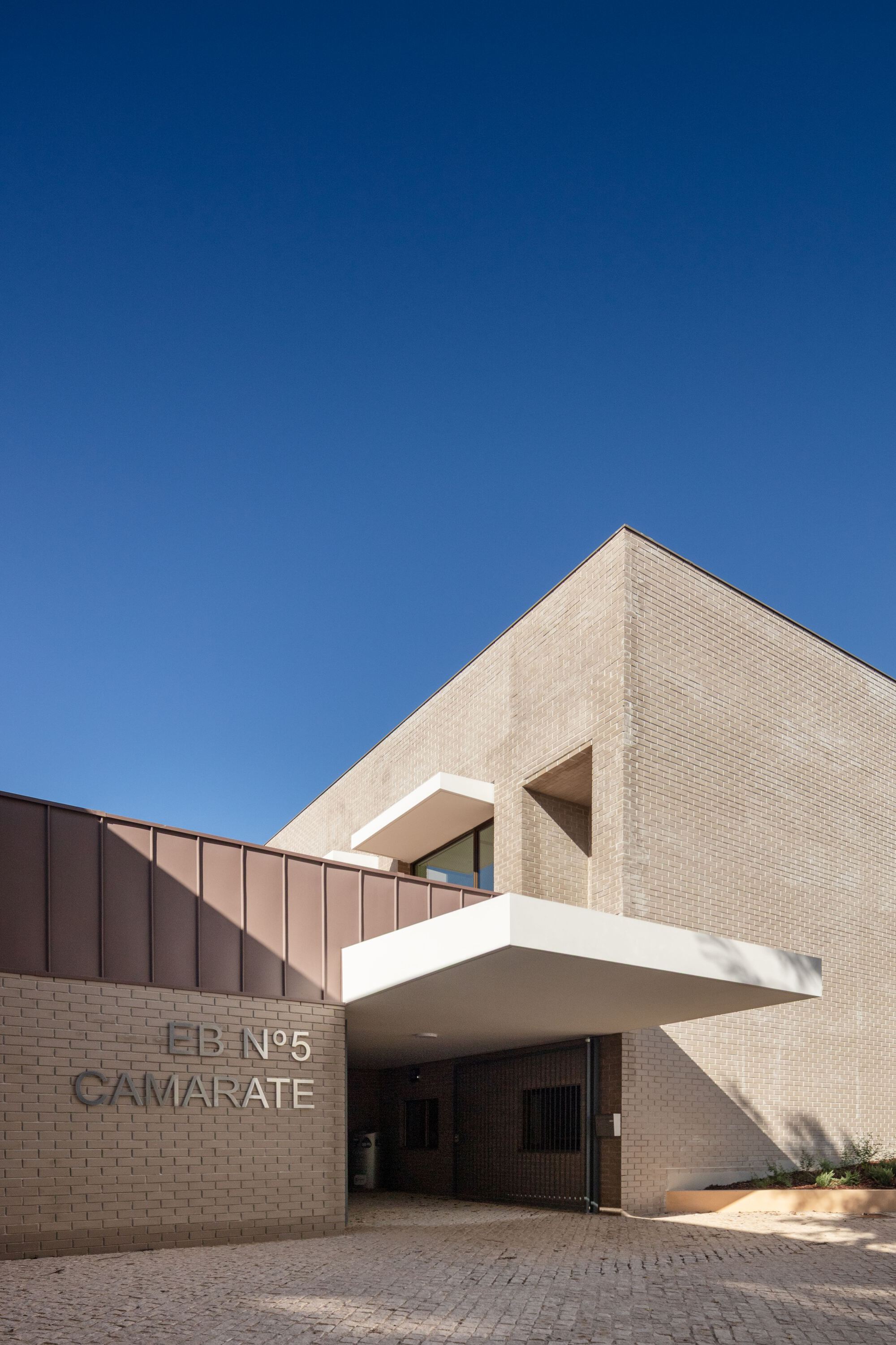 Entrance view with buff brick facade, cantilevered white canopy and copper standing-seam roof under blue sky