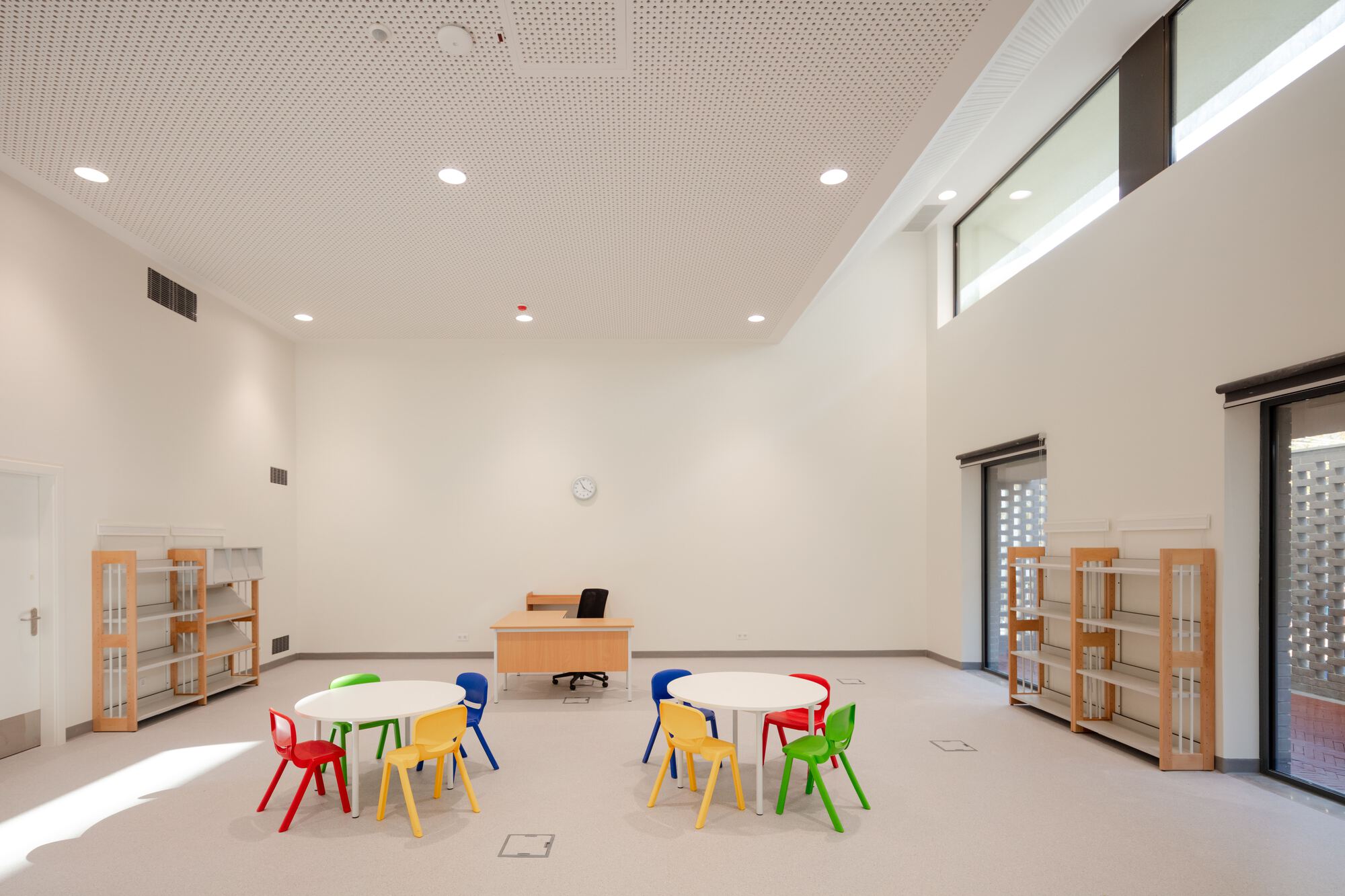Classroom interior with perforated acoustic ceiling and colorful plastic chairs arranged around a central table