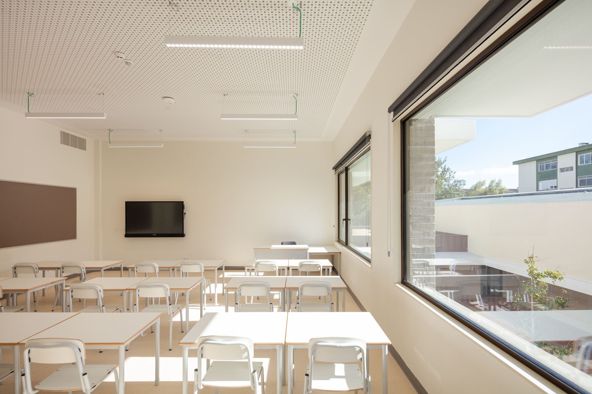 Classroom with white tables and chairs beneath a perforated acoustic ceiling and corner windows