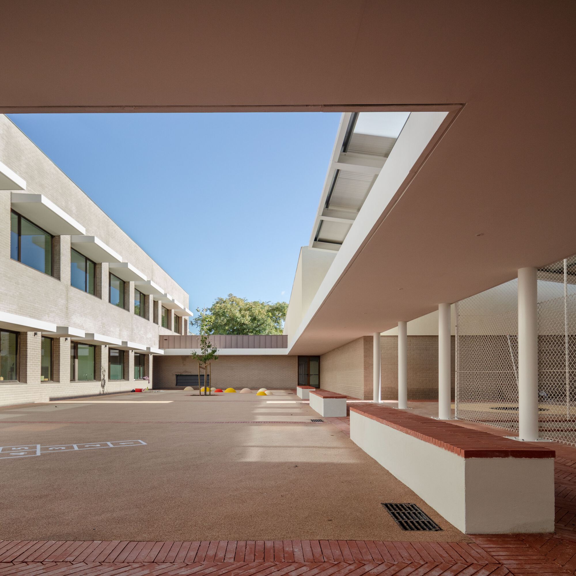 Covered walkway with white columns and red-capped benches framing the courtyard in shade