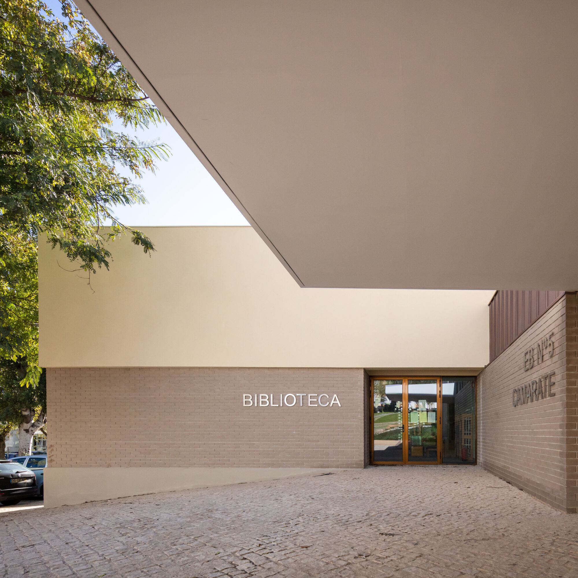 Street-facing entrance with tan brick facade, raised white lettering, and glass doors beneath overhanging volume