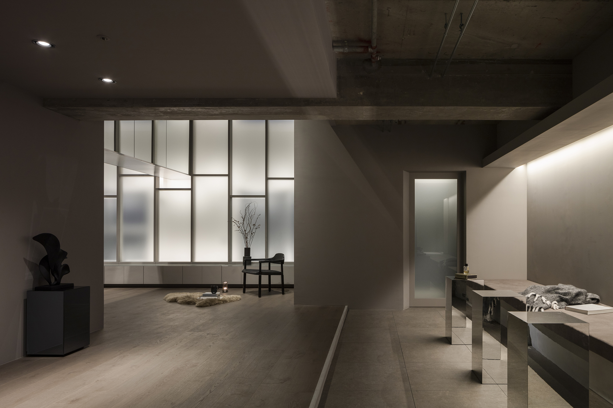 Interior gallery space with backlit translucent glass panels and exposed concrete beam ceiling