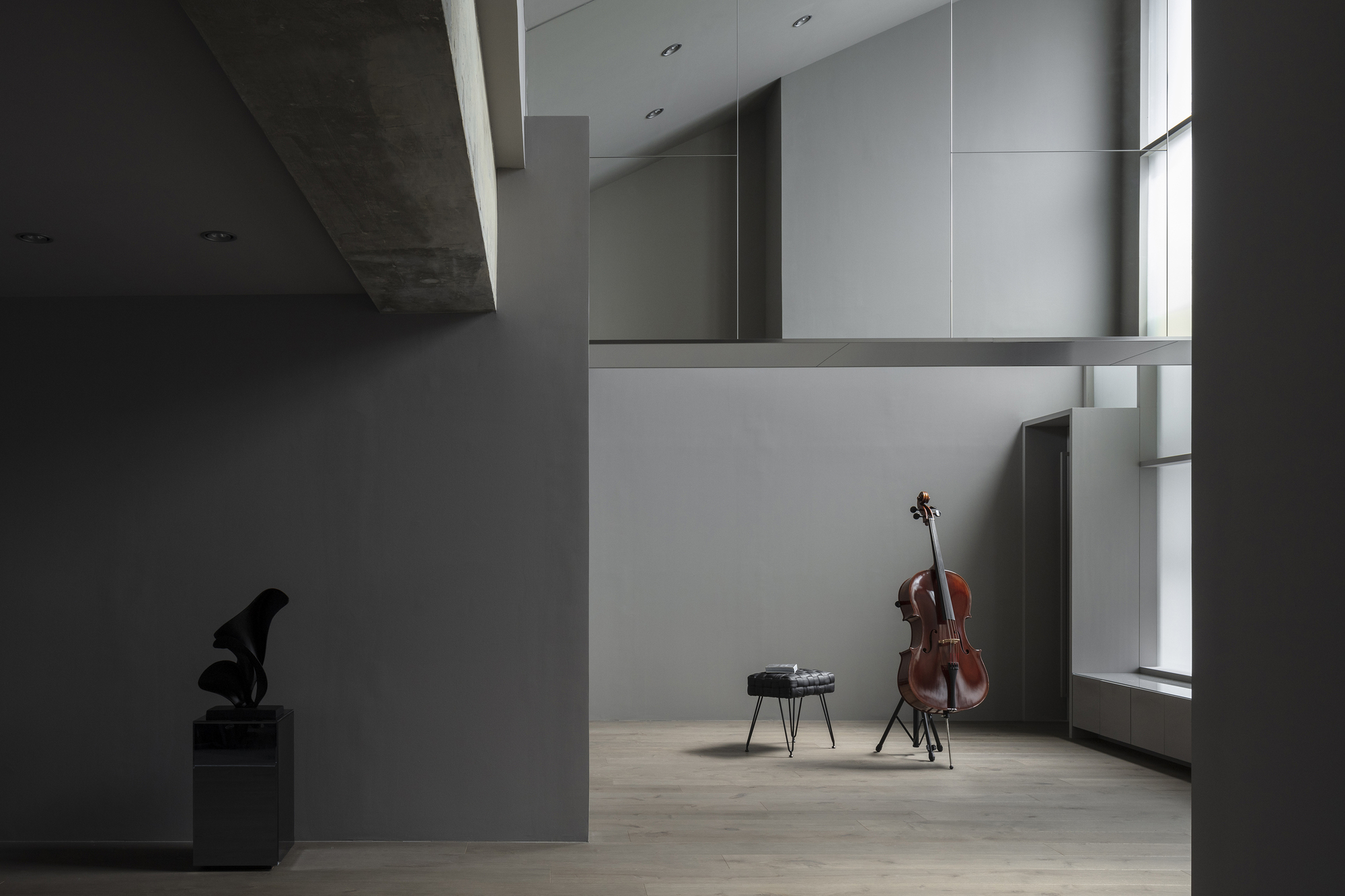 Gallery alcove with cello on stand beside narrow vertical window in grey walls