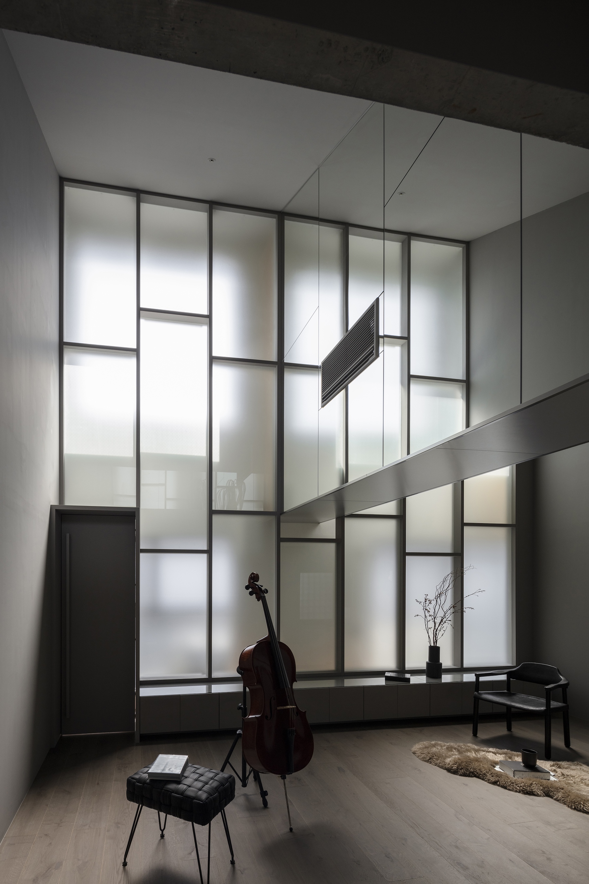 Translucent glass wall with suspended tubular light fixture and horizontal metal beam crossing the frame