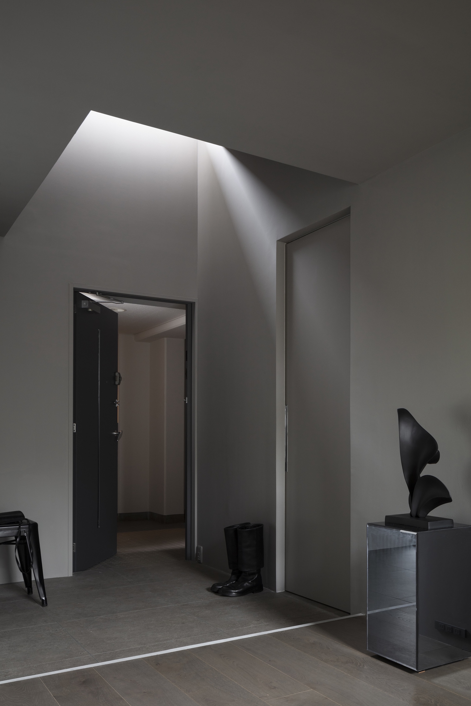 Angled skylight above doorway casting diagonal shadow down pale grey walls and polished floor
