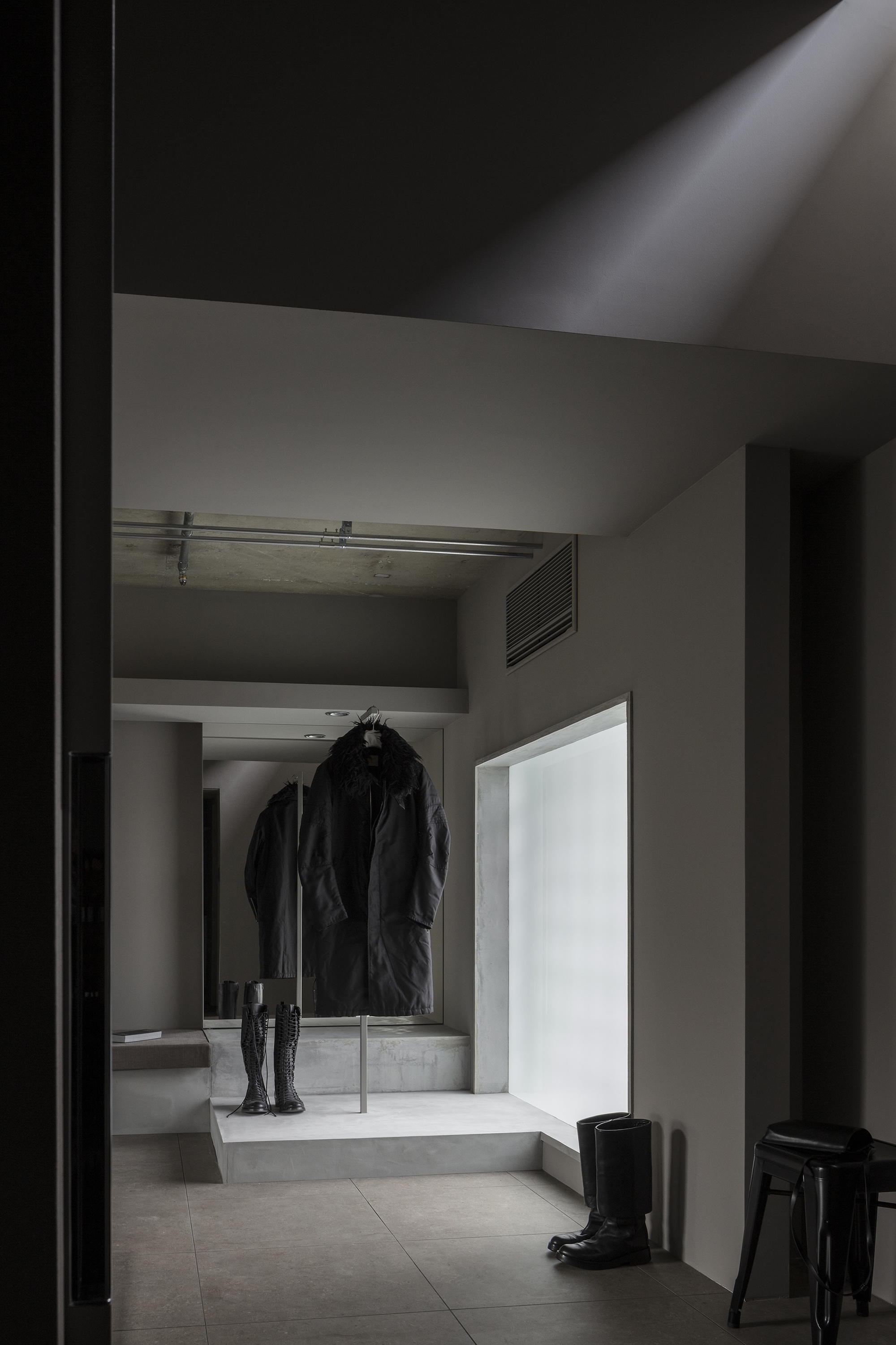 Entry hall with concrete platform displaying coat and boots beneath translucent glass panel