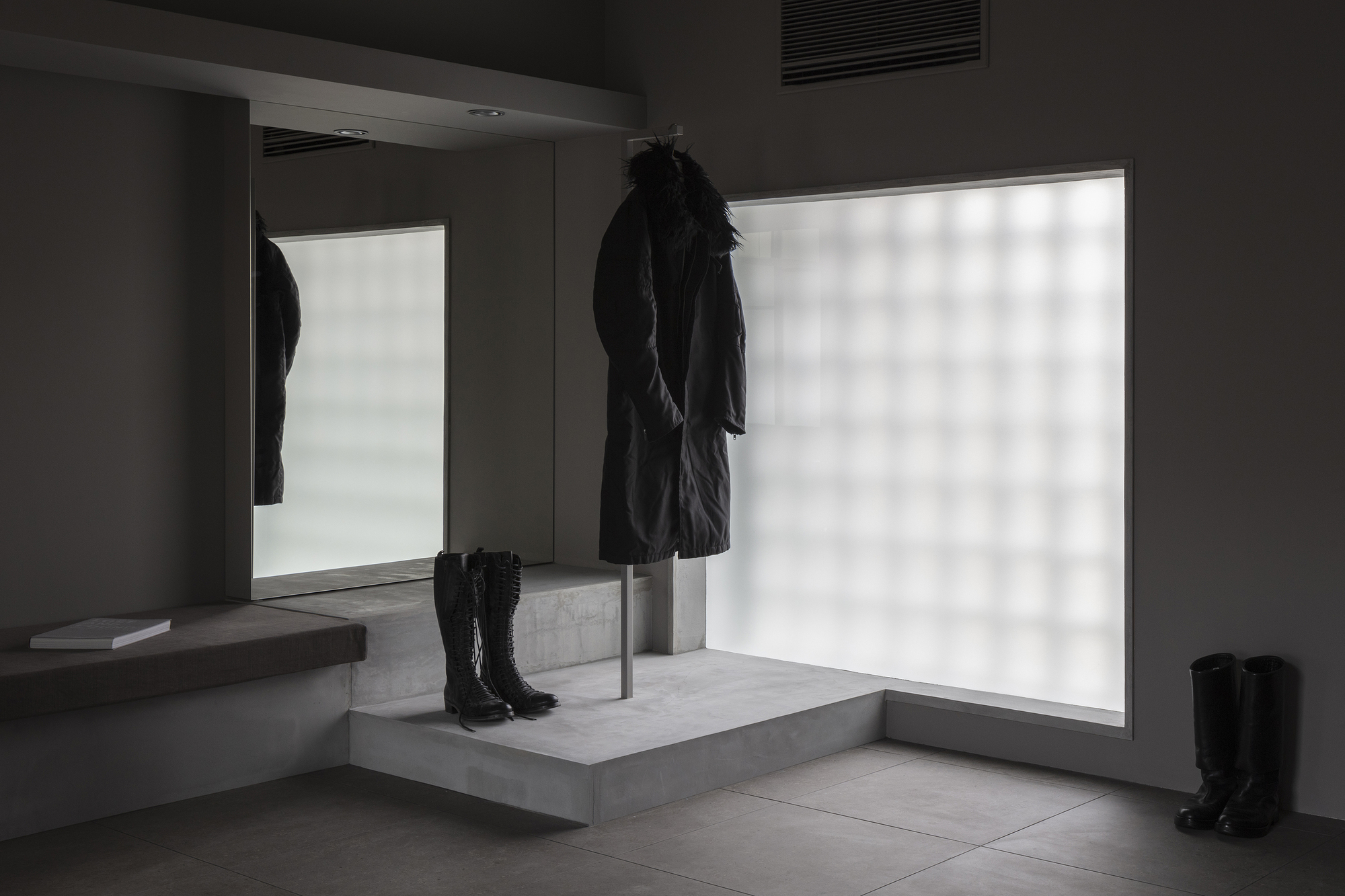 Concrete display pedestal with coat on steel rod and boots against backlit frosted glass