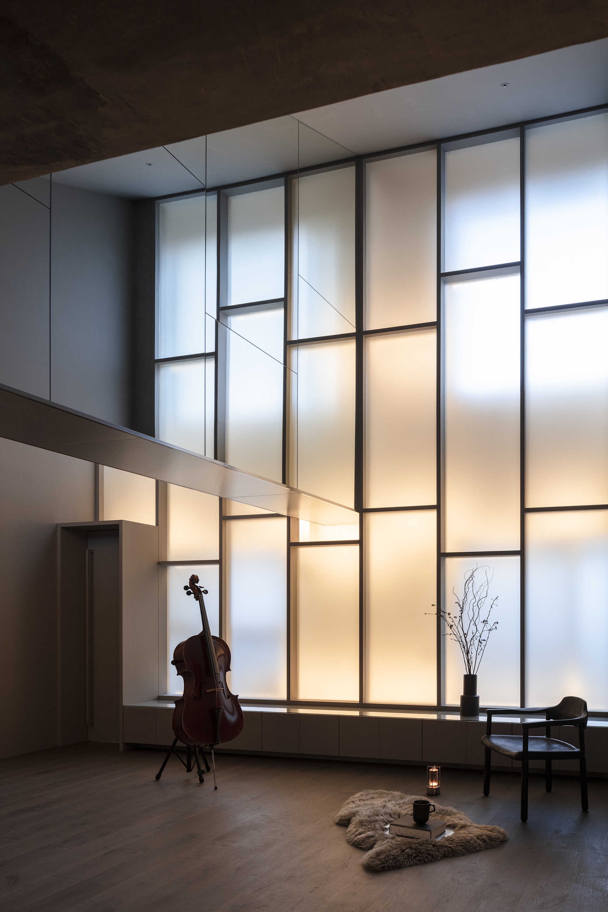 Double-height living space with backlit translucent panel wall and cello in evening light