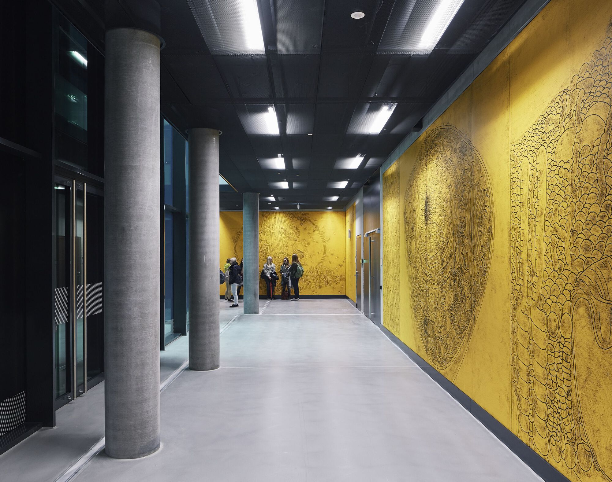 Elevator lobby with circular concrete columns and embossed gold wall panels beside the lift doors