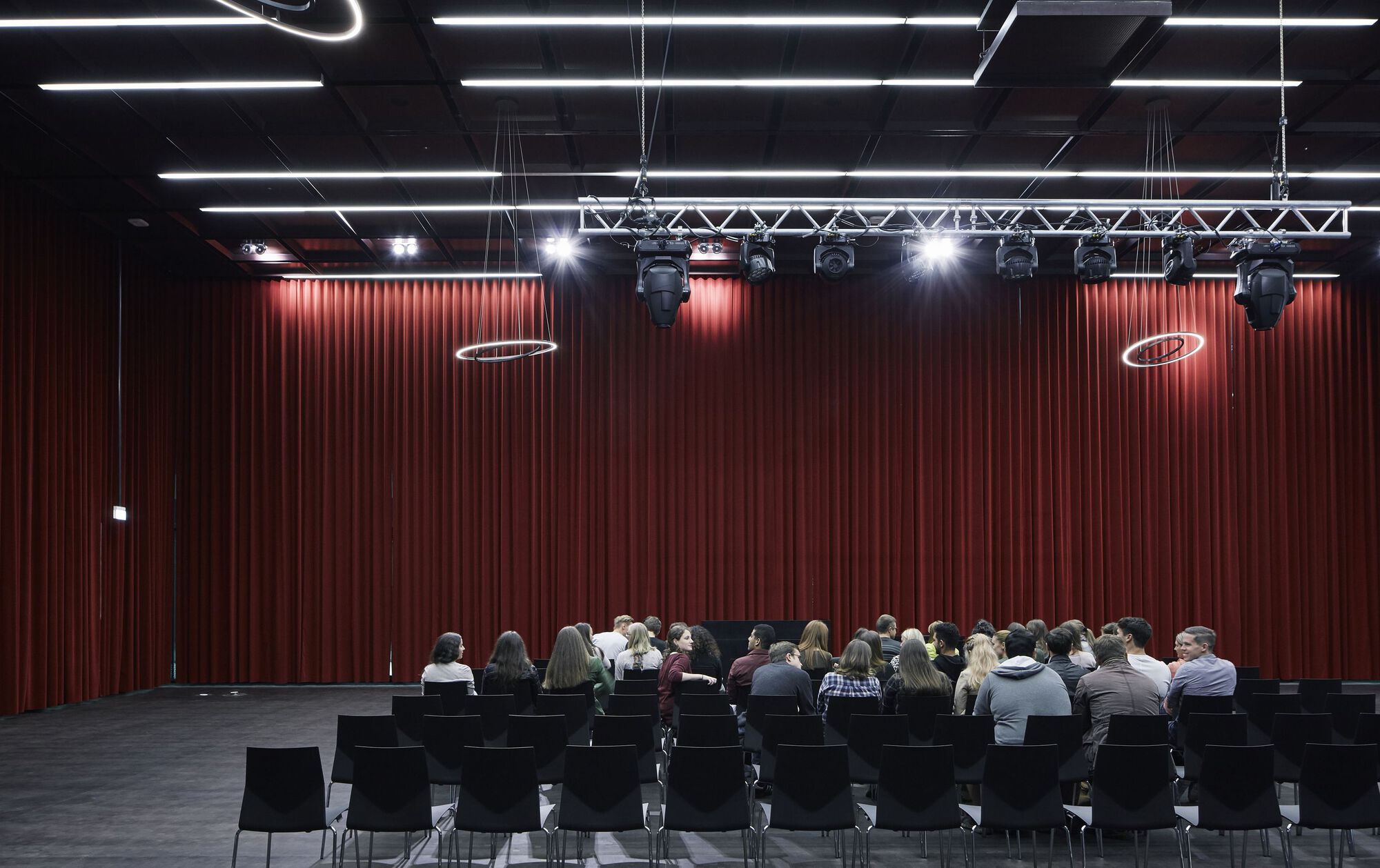 Auditorium with pleated red curtain backdrop and audience seated at rows of black tables