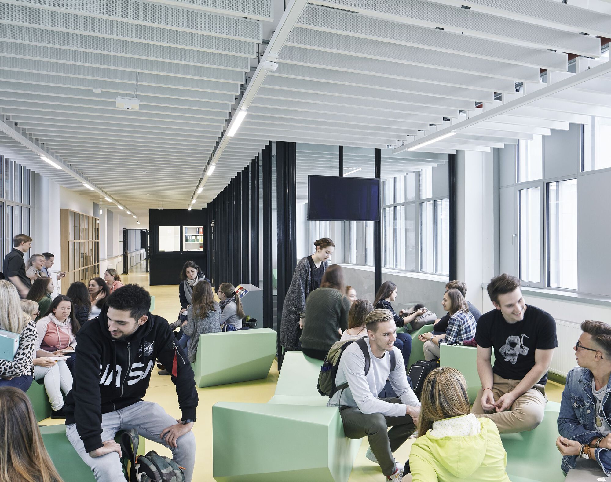 Open lounge space with lime green modular seating and students gathering beneath linear ceiling panels