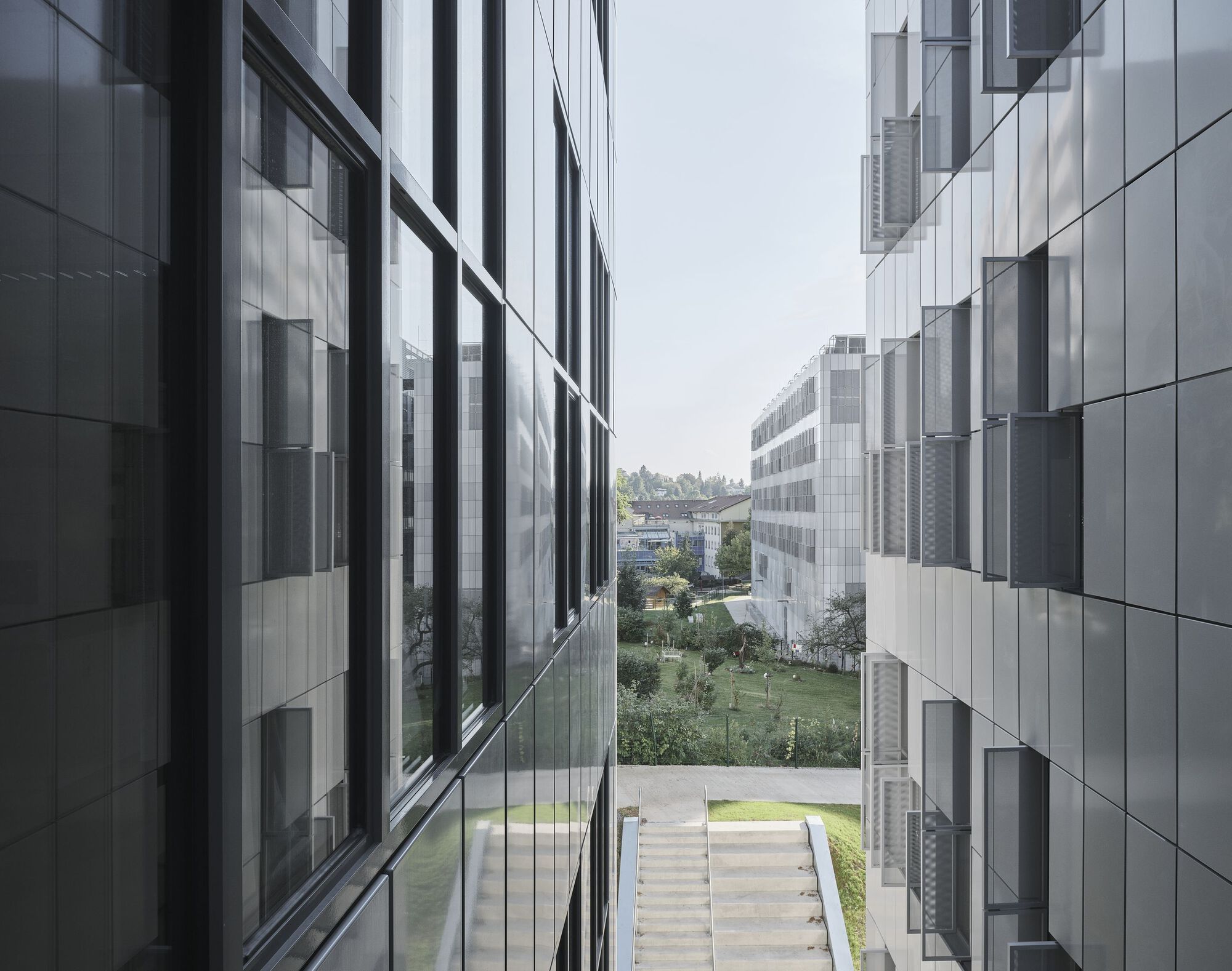 View between two aluminum-clad building volumes framing a landscaped courtyard with central stone steps