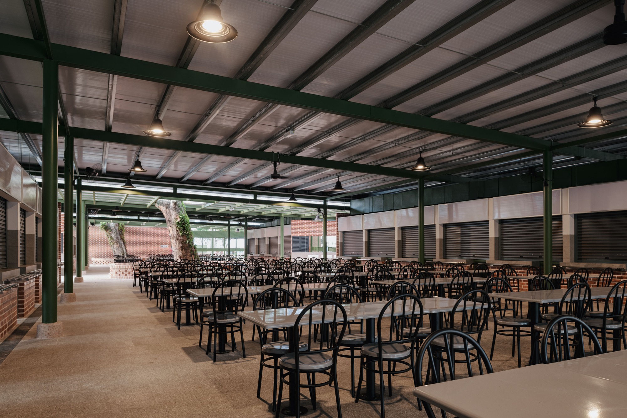 Dining hall interior with rows of tables and chairs under exposed green steel beams and pendant lighting