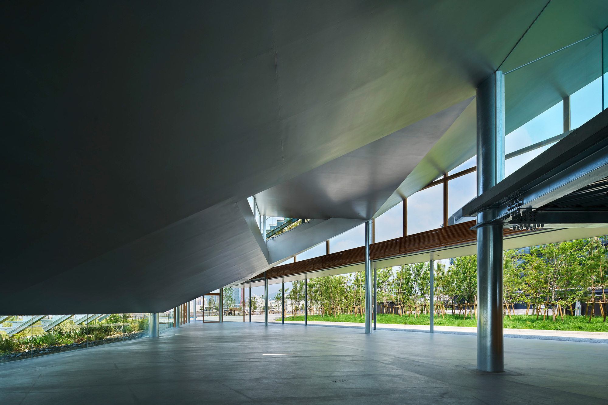 Interior space beneath the sloping roof with steel columns and glazed walls overlooking planted landscape