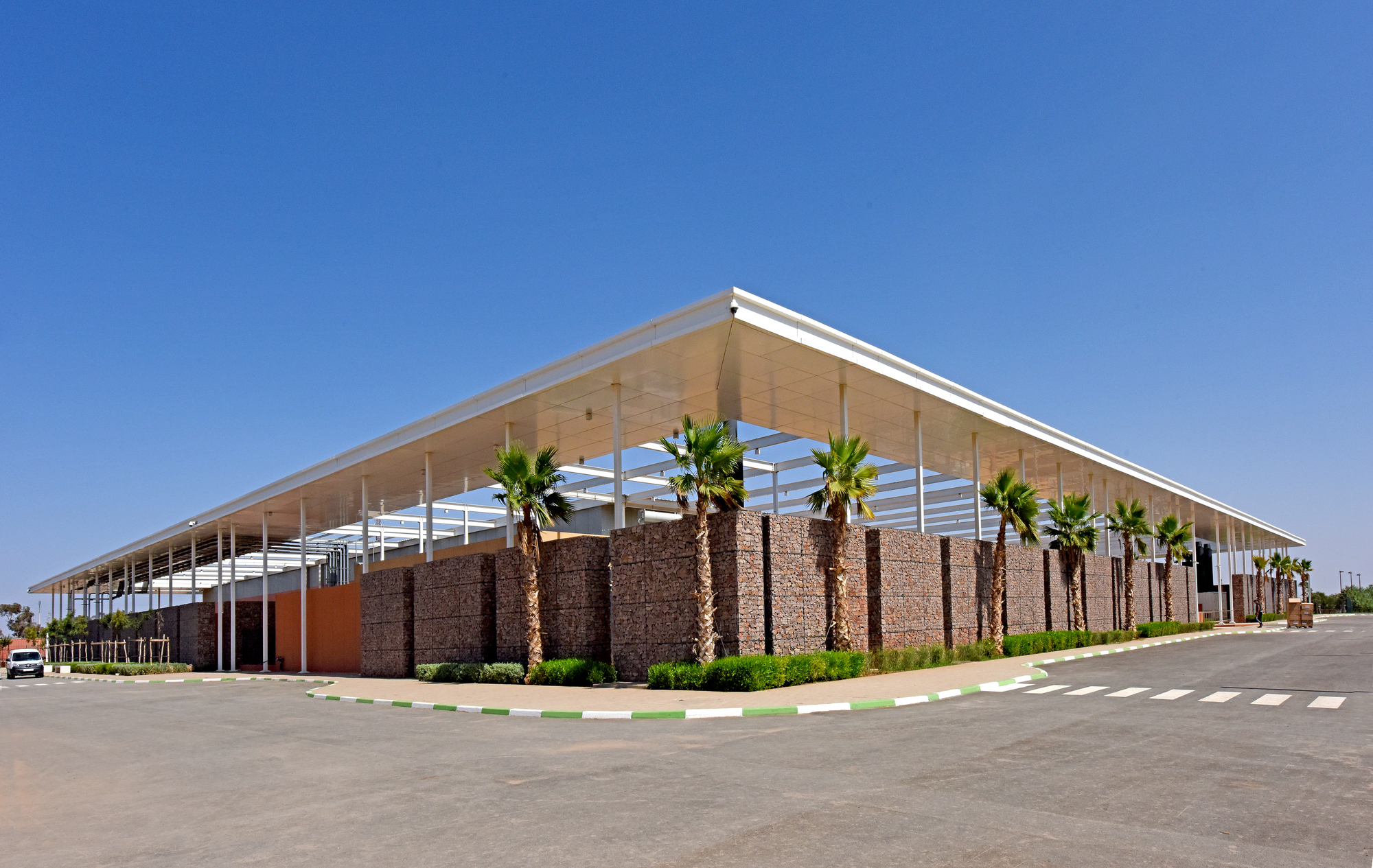 Corner view of the low-slung canopy over gabion walls and palm trees along a paved roadway