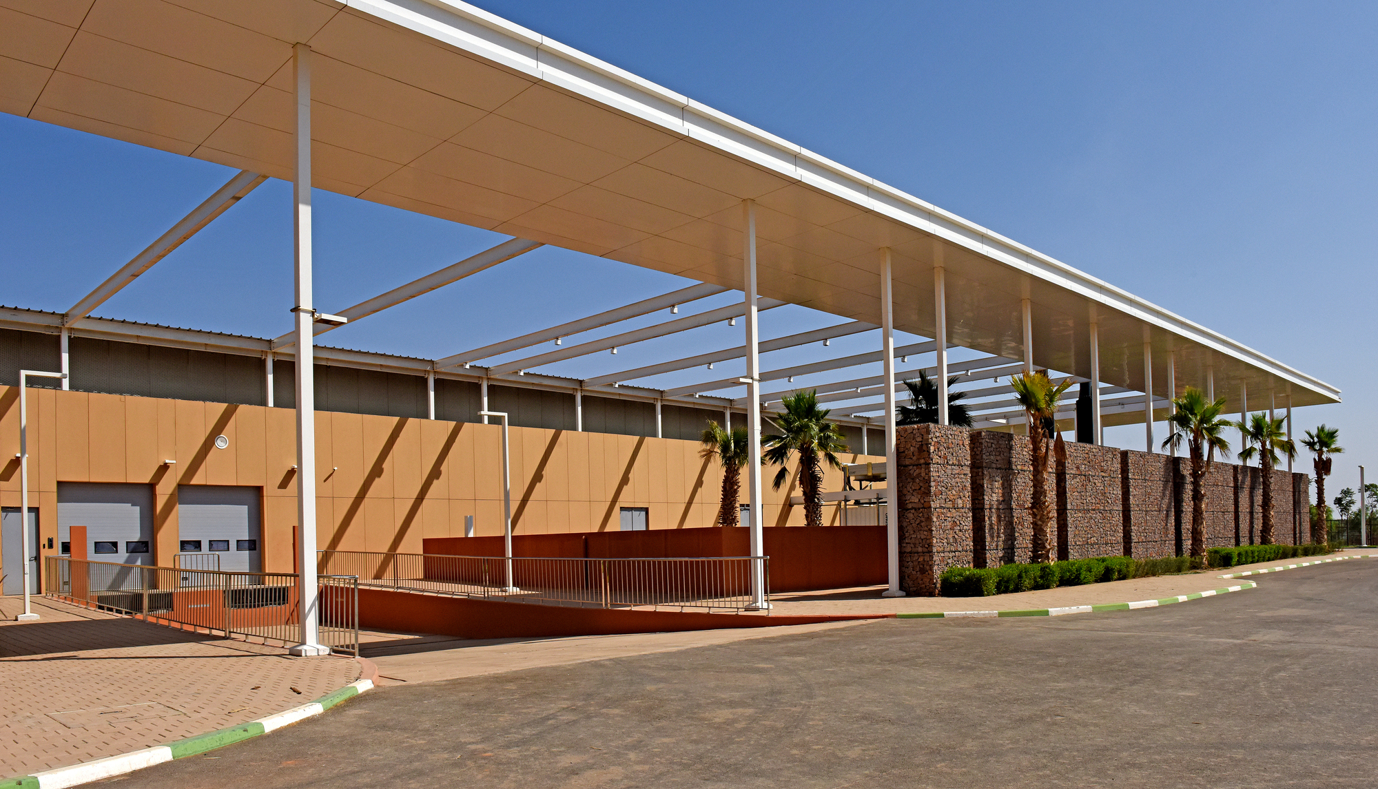 Street view showing the cantilevered canopy with white columns over terracotta panels and gabion walls