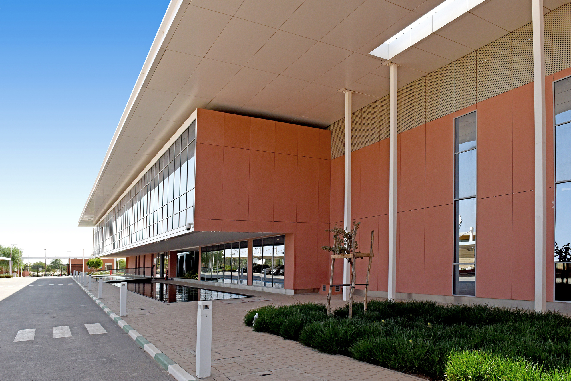 Angled view of the terracotta facade with reflecting pool and perforated metal screens above clerestory glazing